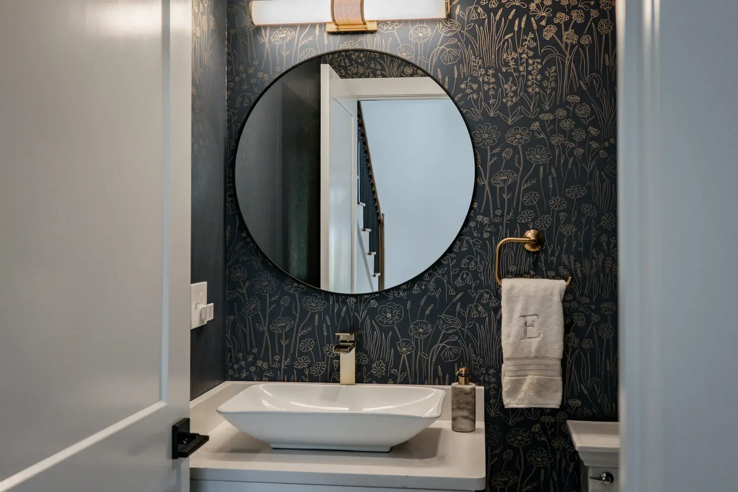 Bathroom remodel with patterned wallpaper, round mirror, and modern fixtures by Bradford Construction.