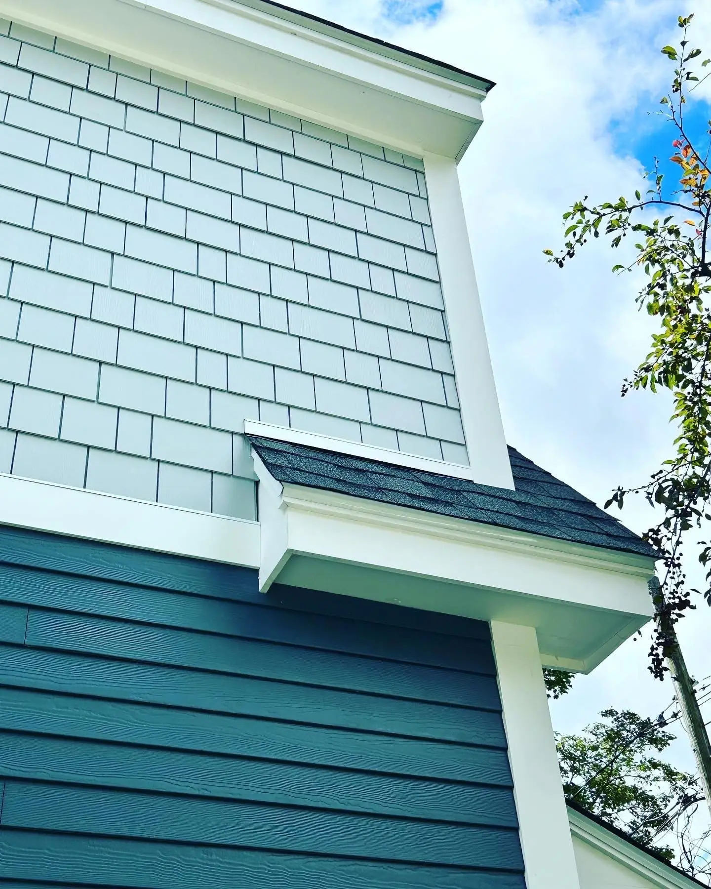 Exterior wall with gray shingle siding and blue horizontal panels, showcasing a modern residential design, complemented by white trim and a clear sky.