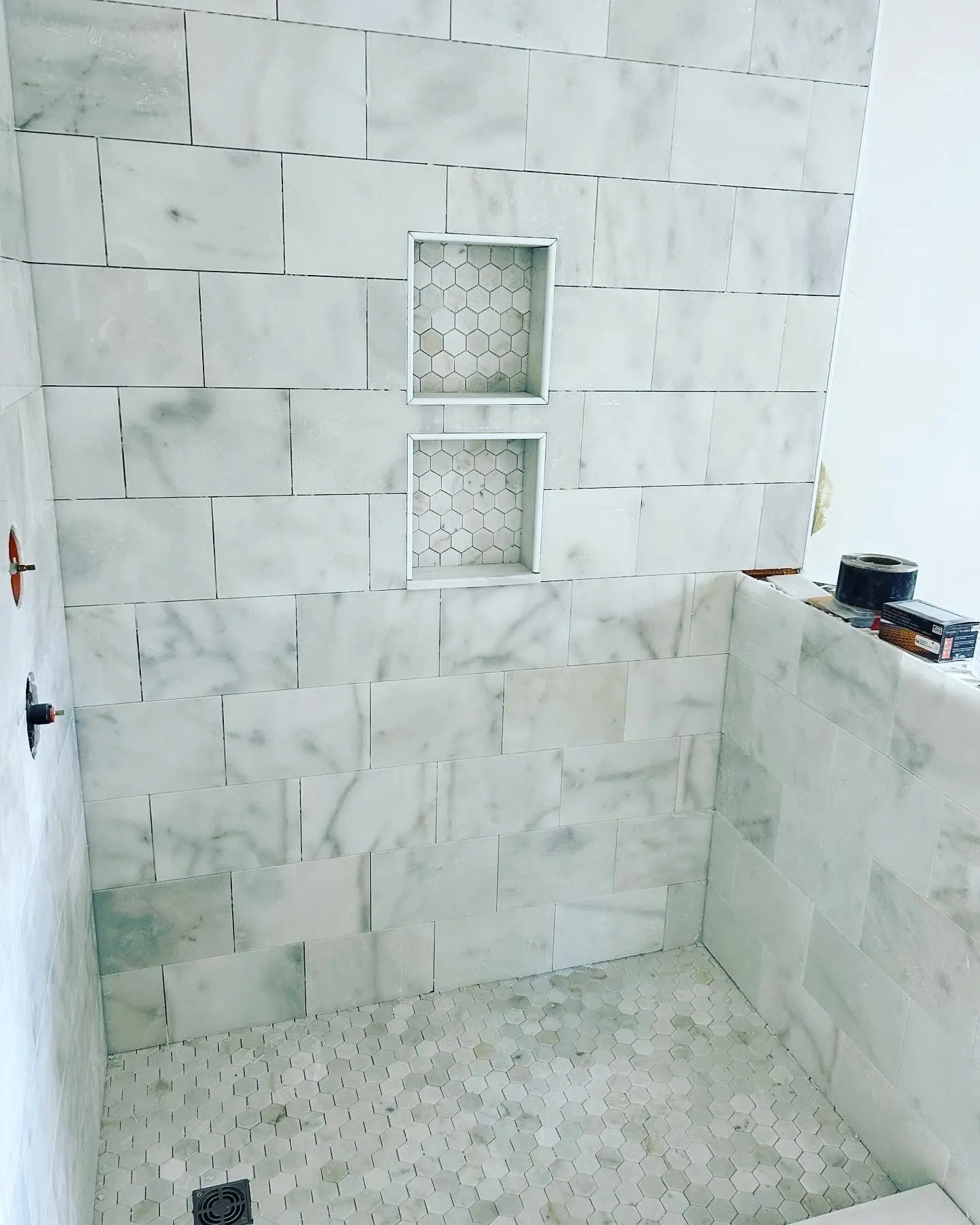 Modern bathroom renovation featuring white marble tile walls and hexagonal floor tiles, showcasing built-in niche for storage, highlighting Bradford Construction Management's design capabilities.