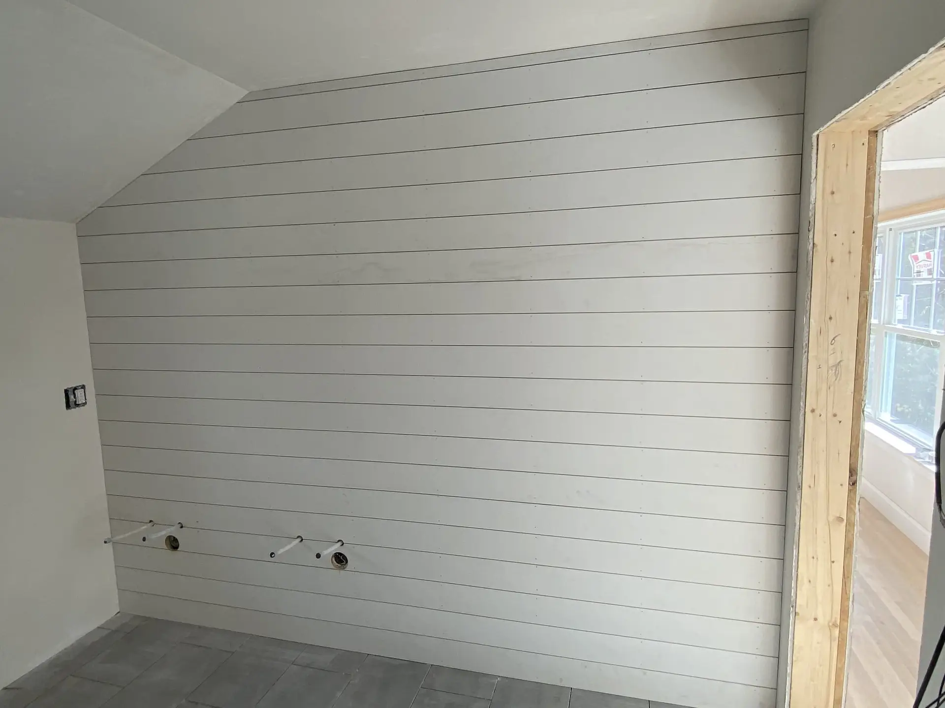 Interior view of a newly renovated room featuring a shiplap wall, unfinished plumbing fixtures, and a doorway leading to a well-lit area, showcasing Bradford Construction Management's home renovation work.