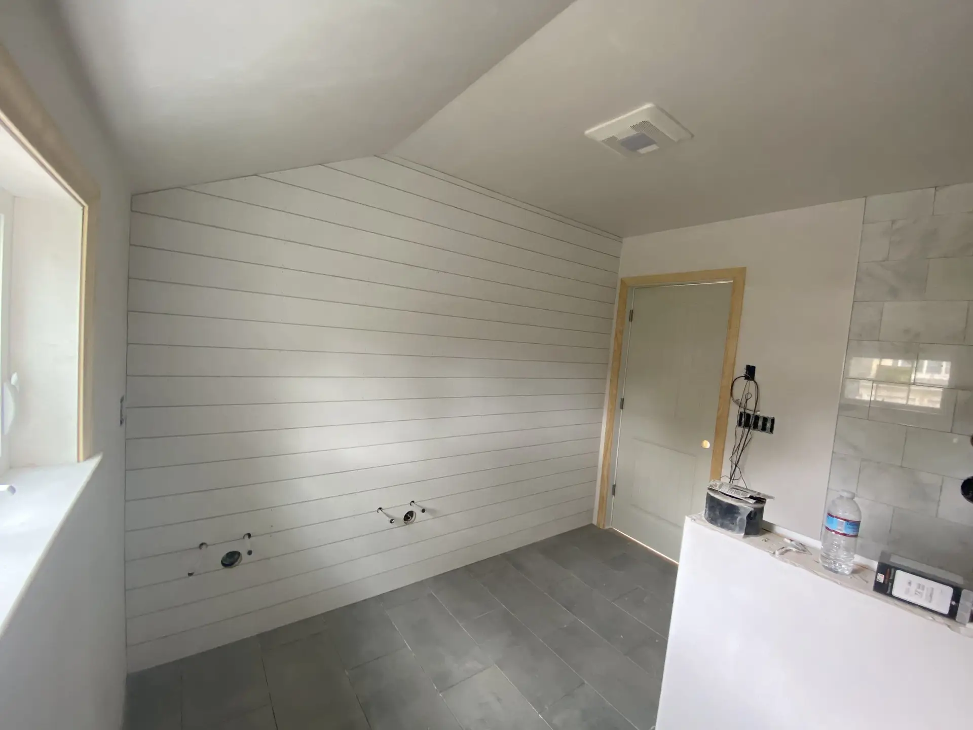 Interior view of a renovated room featuring shiplap walls, a light-colored door, and gray tile flooring, showcasing the quality craftsmanship of Bradford Construction Management's home renovation services in South Hamilton, MA.