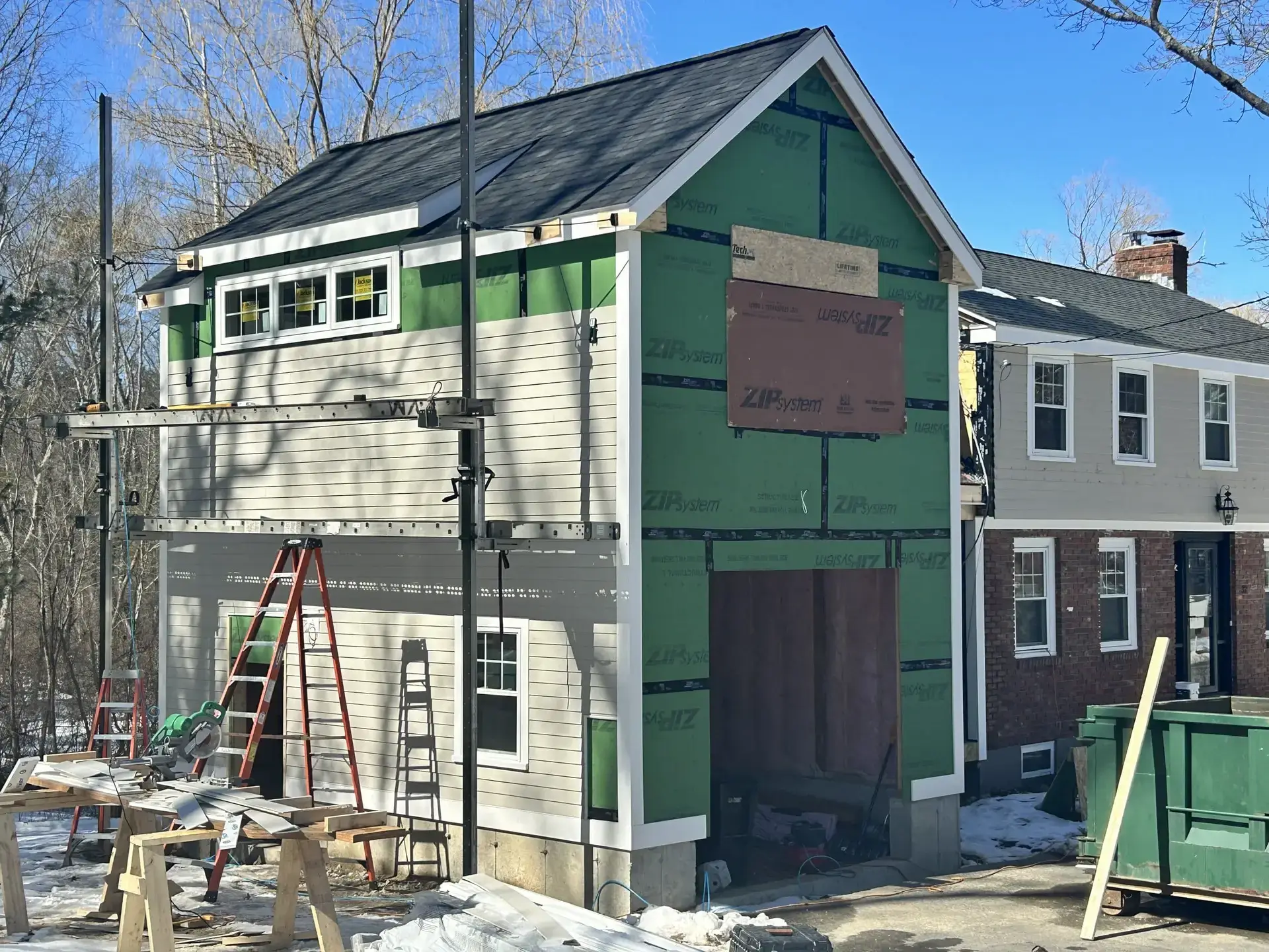 Home addition construction in South Hamilton, featuring scaffolding, ladders, and partially finished exterior with ZIP System sheathing.