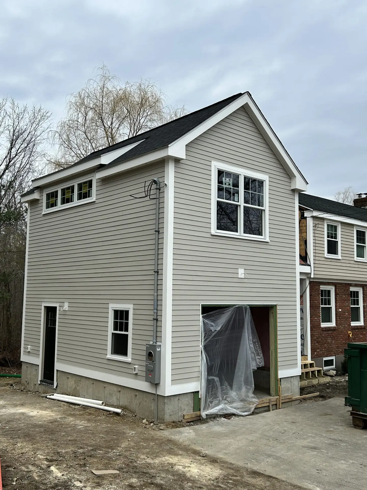 Newly constructed accessory dwelling unit in South Hamilton, MA, featuring modern design elements, gray siding, multiple windows, and a garage space under construction.