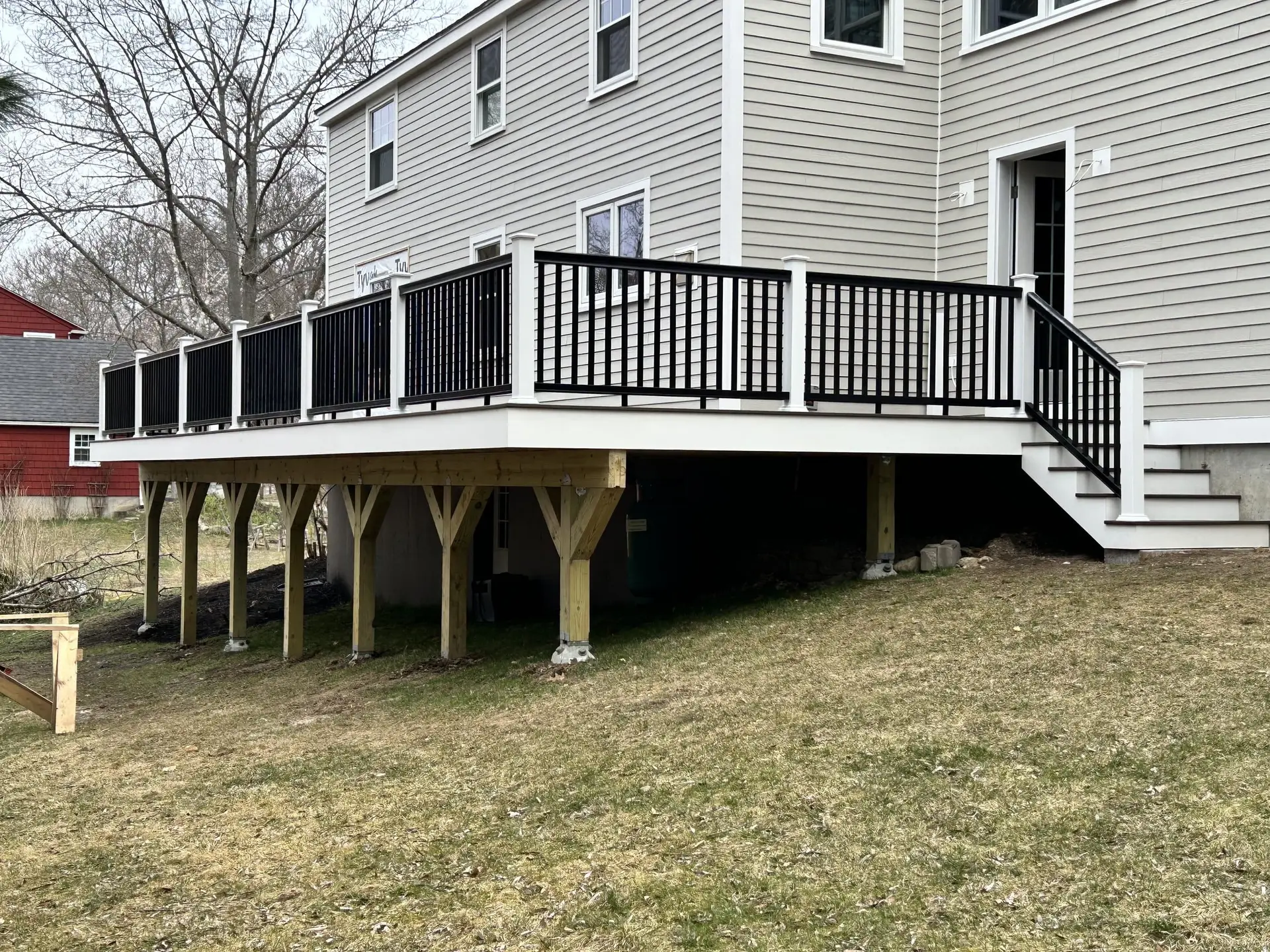 Newly constructed deck with black railing and stairs, attached to a modern home in South Hamilton, MA, showcasing quality craftsmanship by Bradford Construction Management.