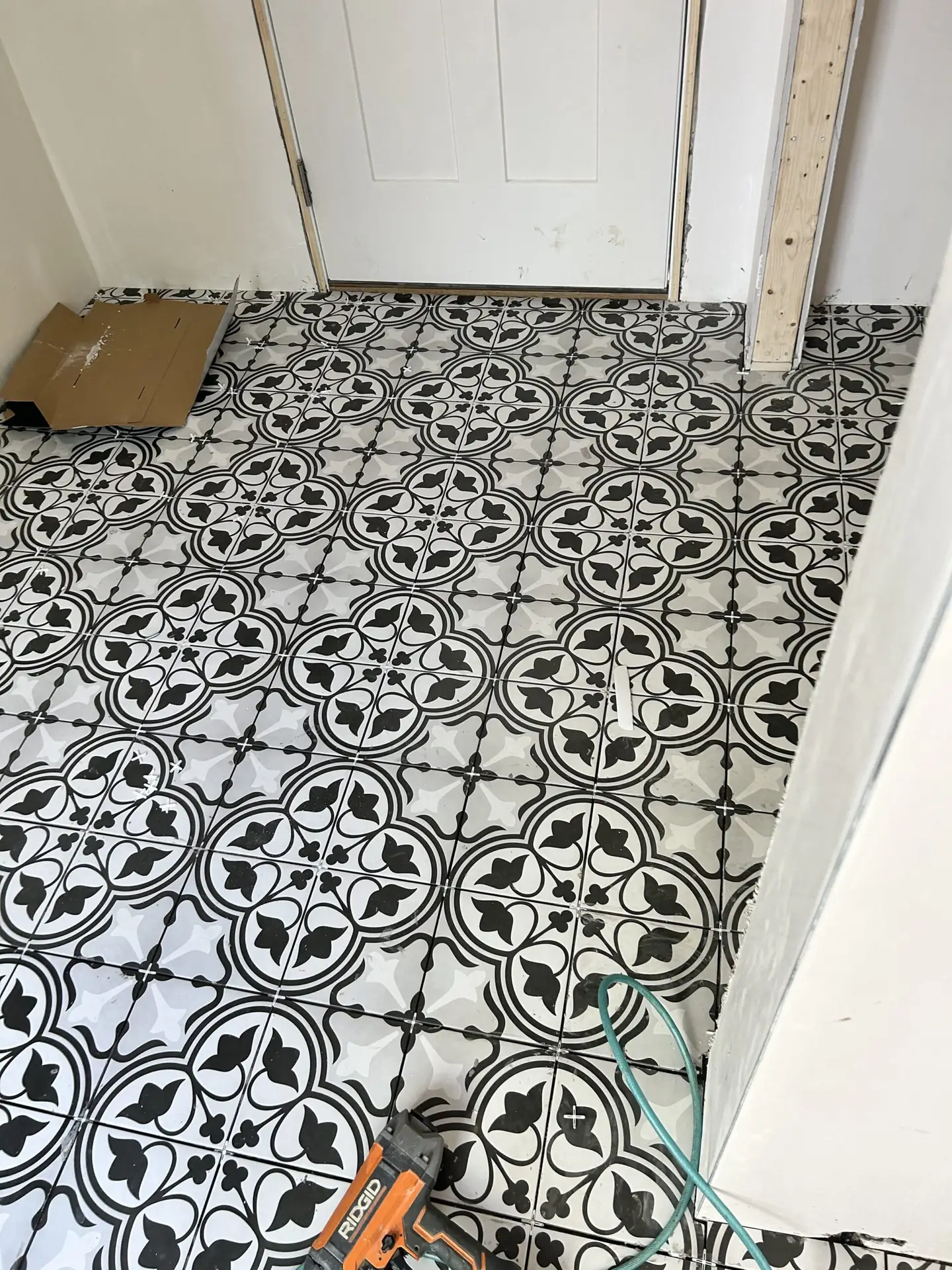 Black and white patterned tile flooring in a home entryway, featuring a door and construction tools, showcasing a renovation project by Bradford Construction Management in South Hamilton, MA.