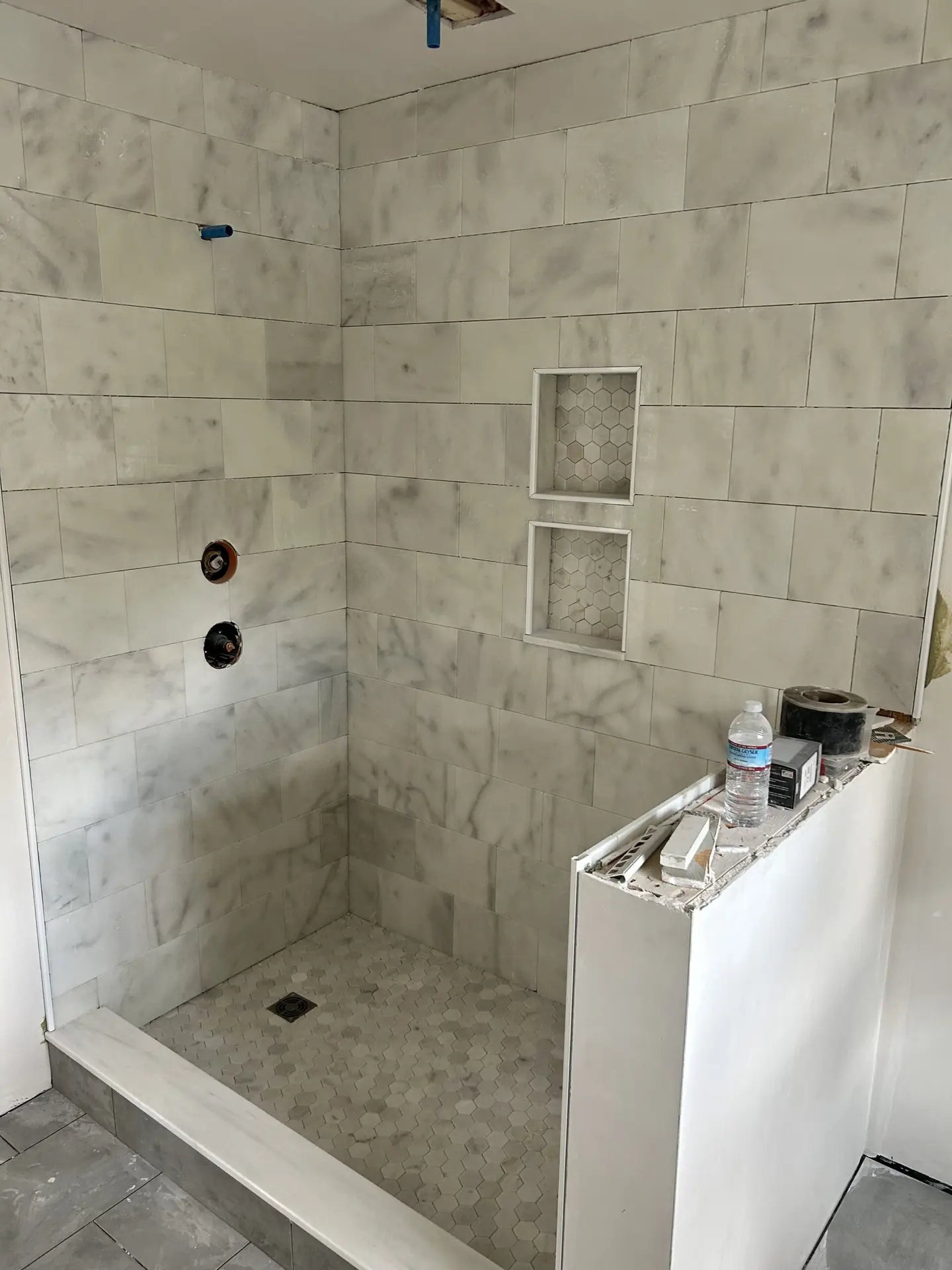 Renovated shower space featuring marble tile walls, hexagonal tile flooring, and recessed shelving, showcasing Bradford Construction Management's quality craftsmanship in home renovations.
