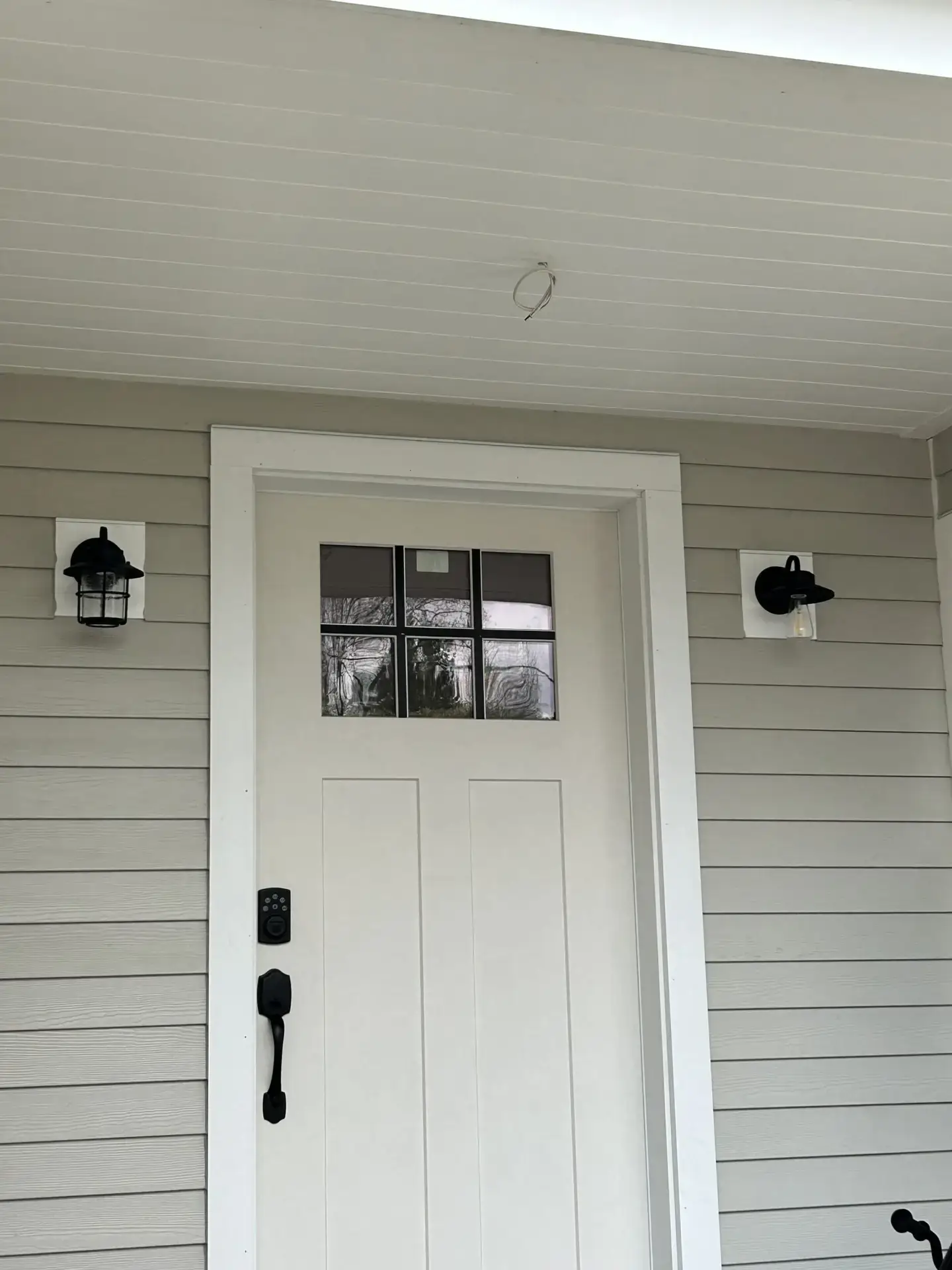 Front entrance of a custom home featuring a white door with glass panels, modern black door hardware, and wall-mounted lighting fixtures, highlighting residential construction details.