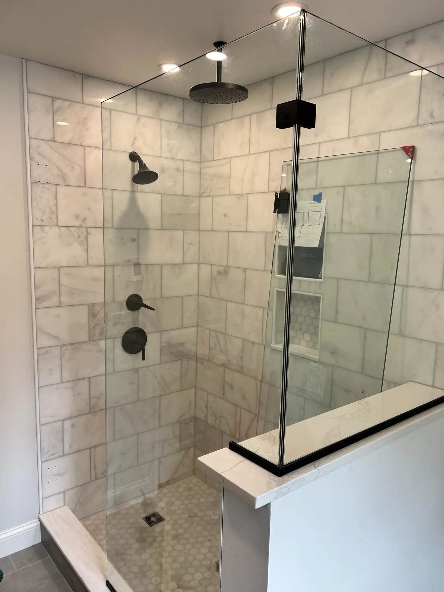 Modern glass shower enclosure with marble tiled walls and hexagonal floor tiles, showcasing sleek fixtures and a contemporary design, reflecting Bradford Construction Management's quality renovations in South Hamilton, MA.