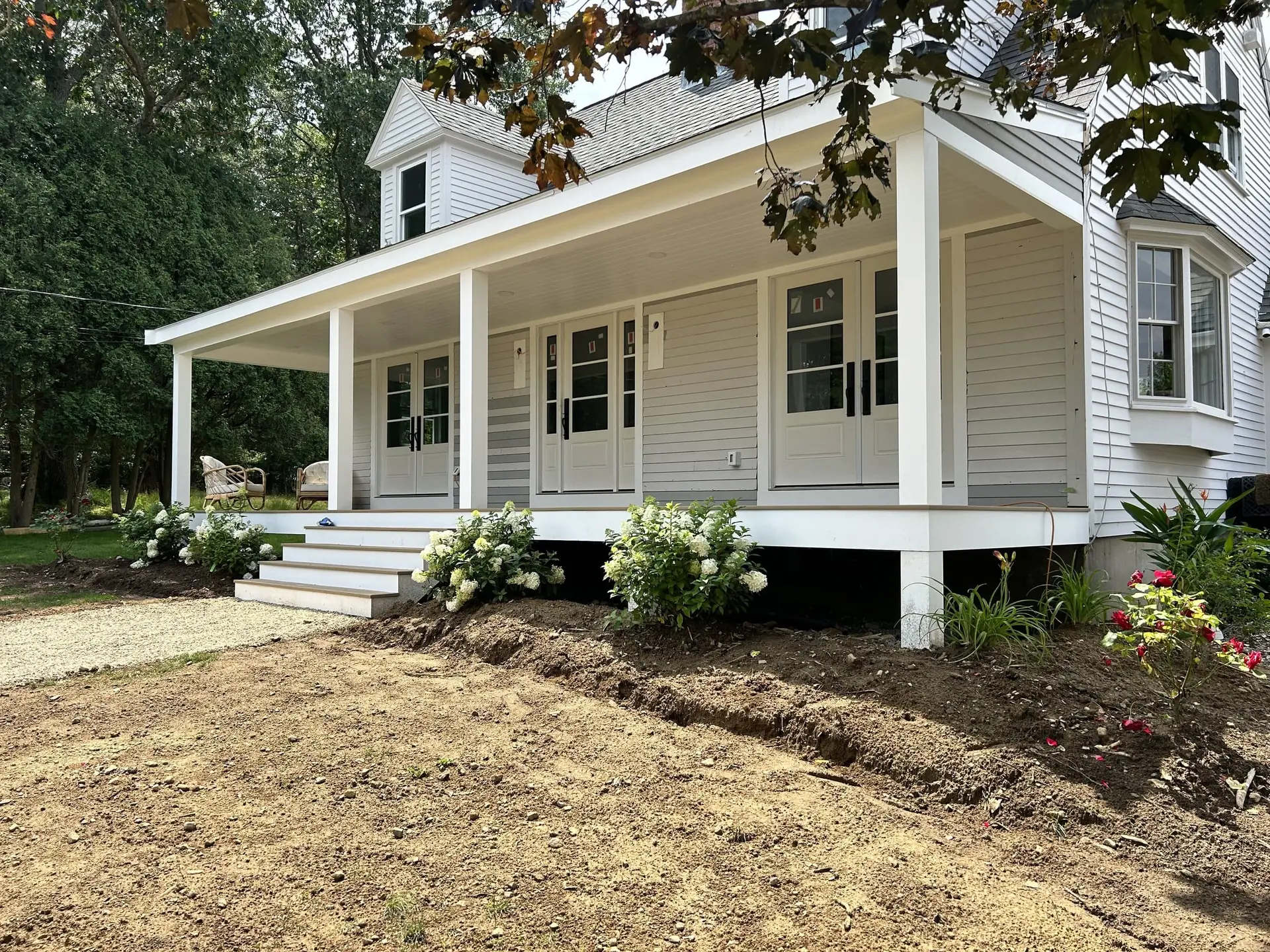 Custom home exterior in Wakefield, MA featuring a farmer's porch, white clapboard siding, landscaped front yard with hydrangeas, and new foundation steps.