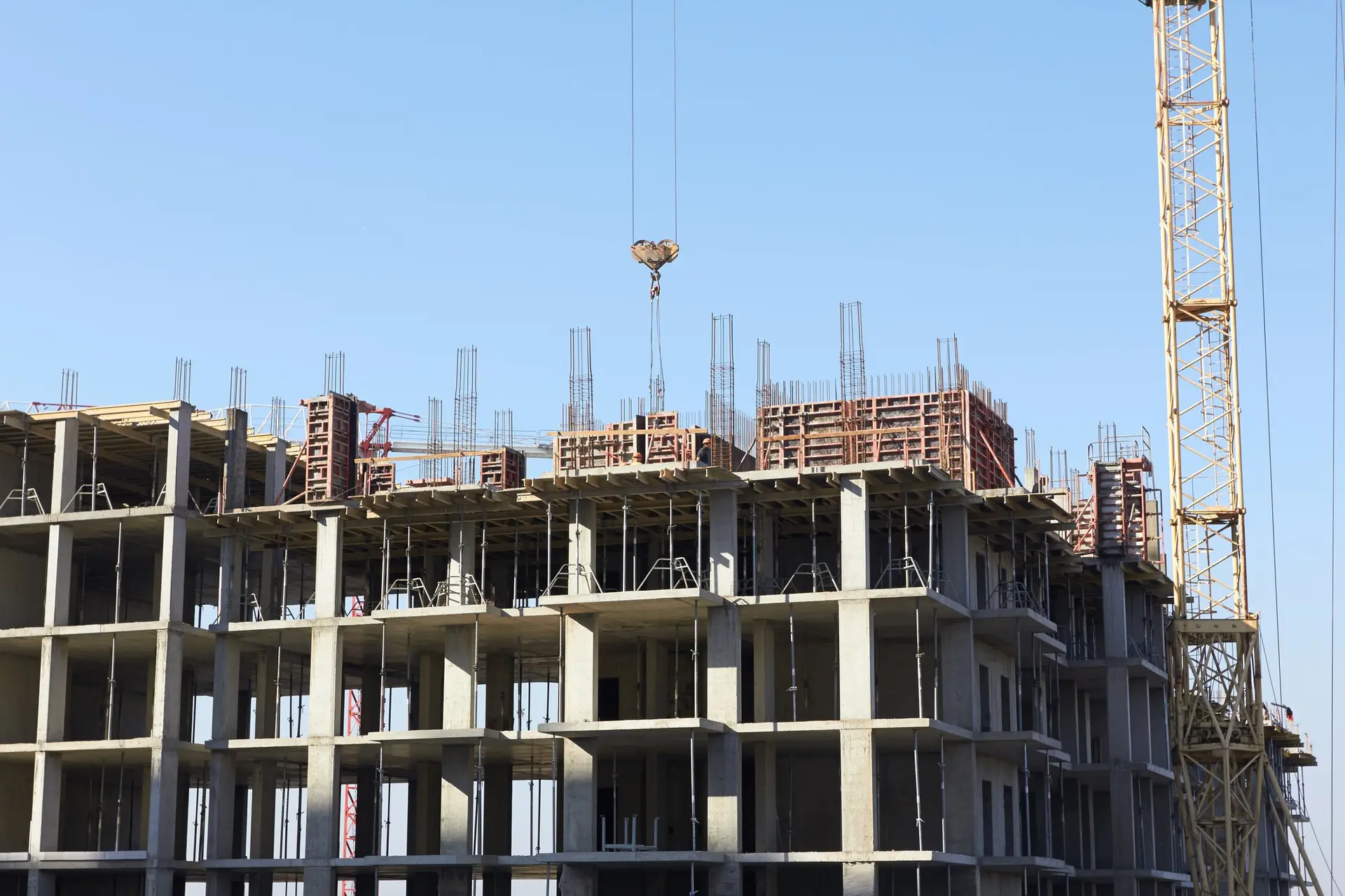 Construction site featuring a crane lifting materials, with a partially built concrete structure and scaffolding, indicative of commercial construction projects managed by Bradford Construction.