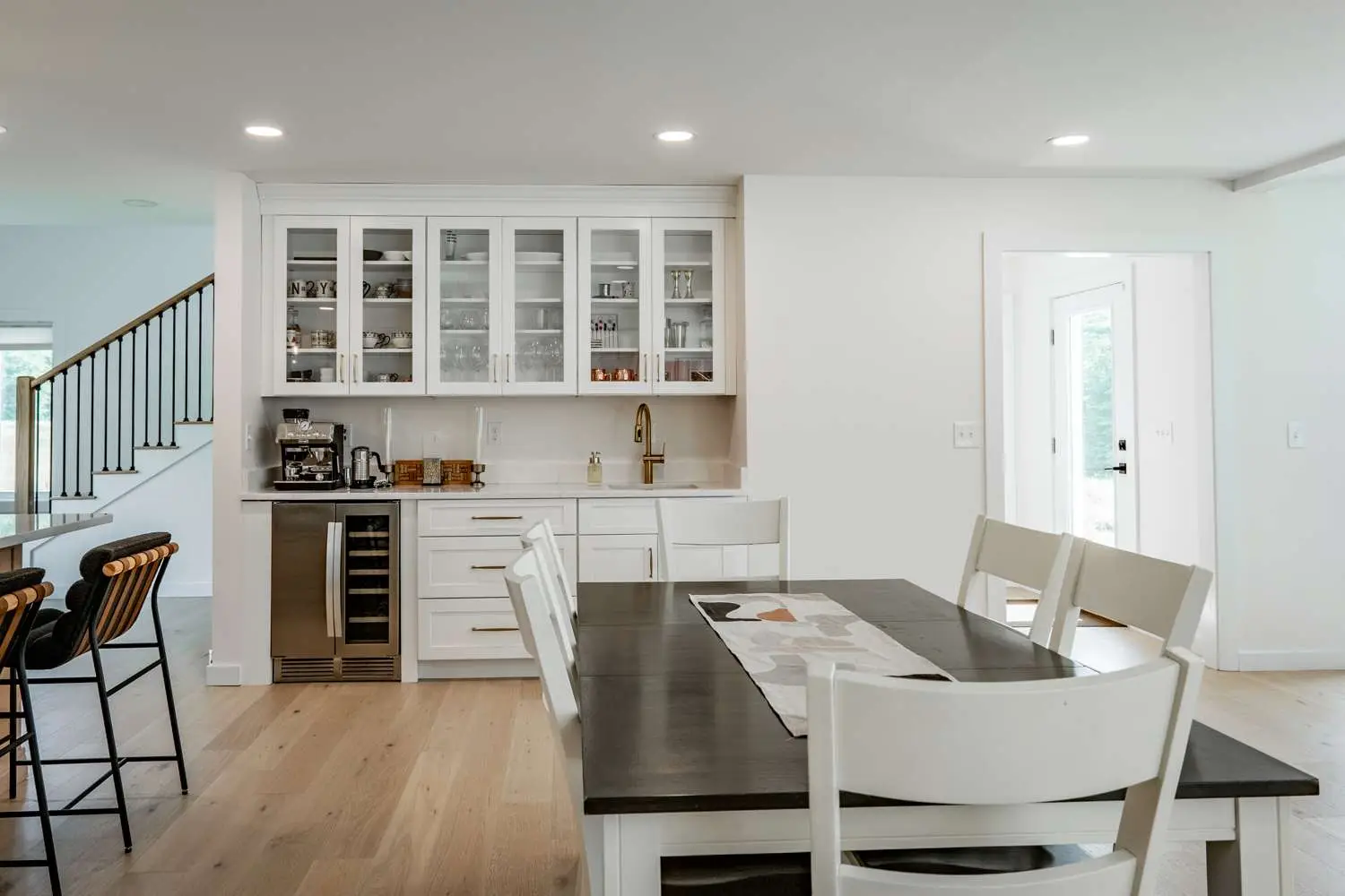 Modern kitchen interior featuring white cabinetry, a sleek countertop with a wine cooler, and a dining table with a decorative runner, highlighting energy-efficient design elements for custom homes by Bradford Construction Management.