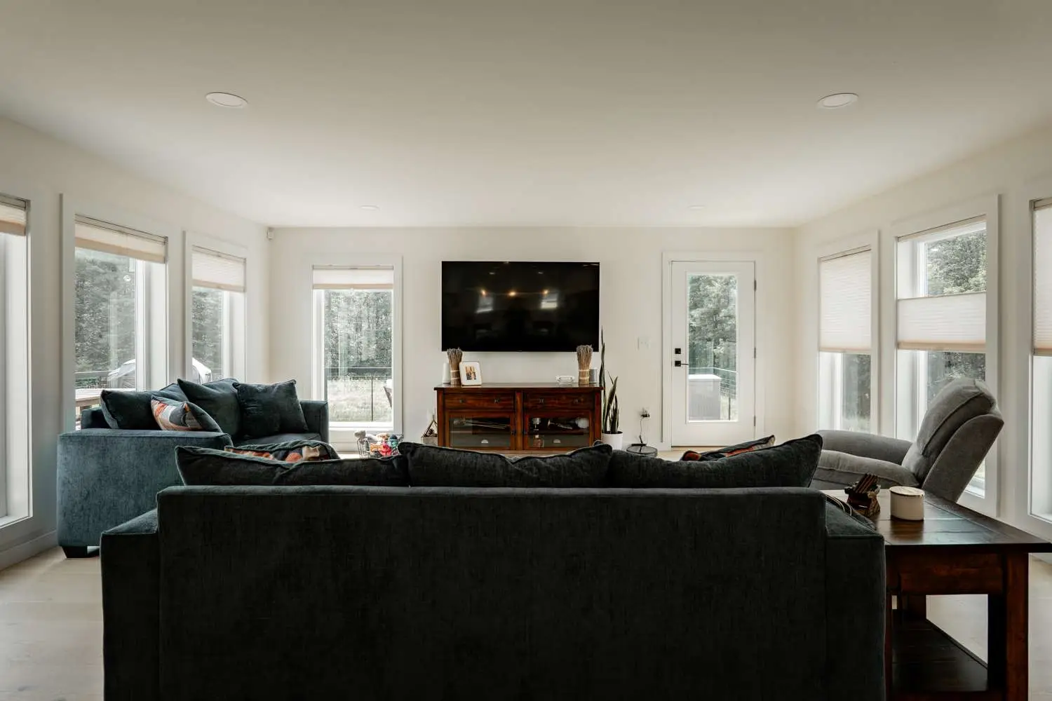 Modern living room with energy-efficient design, featuring plush sofas, a wooden TV stand, and large windows for natural light, emphasizing Bradford Construction Management's focus on high-performance homes.