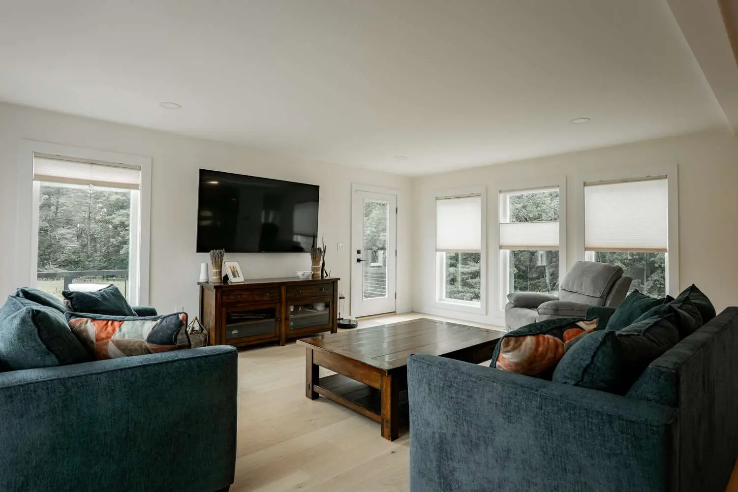 Modern living room with teal sofas, wooden coffee table, large flat-screen TV, and natural light from multiple windows, showcasing a cozy atmosphere ideal for custom home designs.