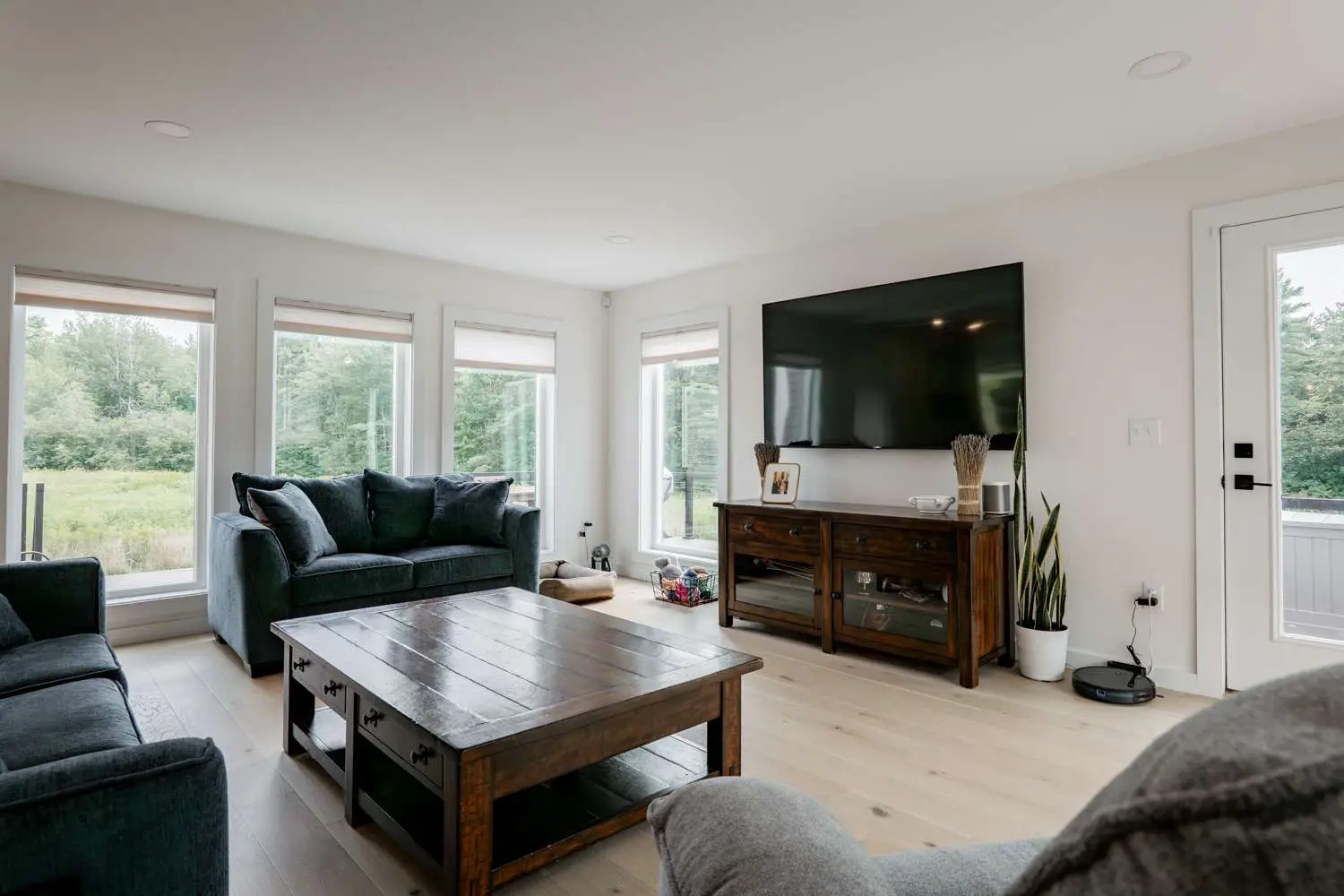 Cozy living room featuring a dark blue sofa set, wooden coffee table, large flat-screen TV, and floor-to-ceiling windows with views of greenery, showcasing custom home design by Bradford Construction Management in Exeter, NH.