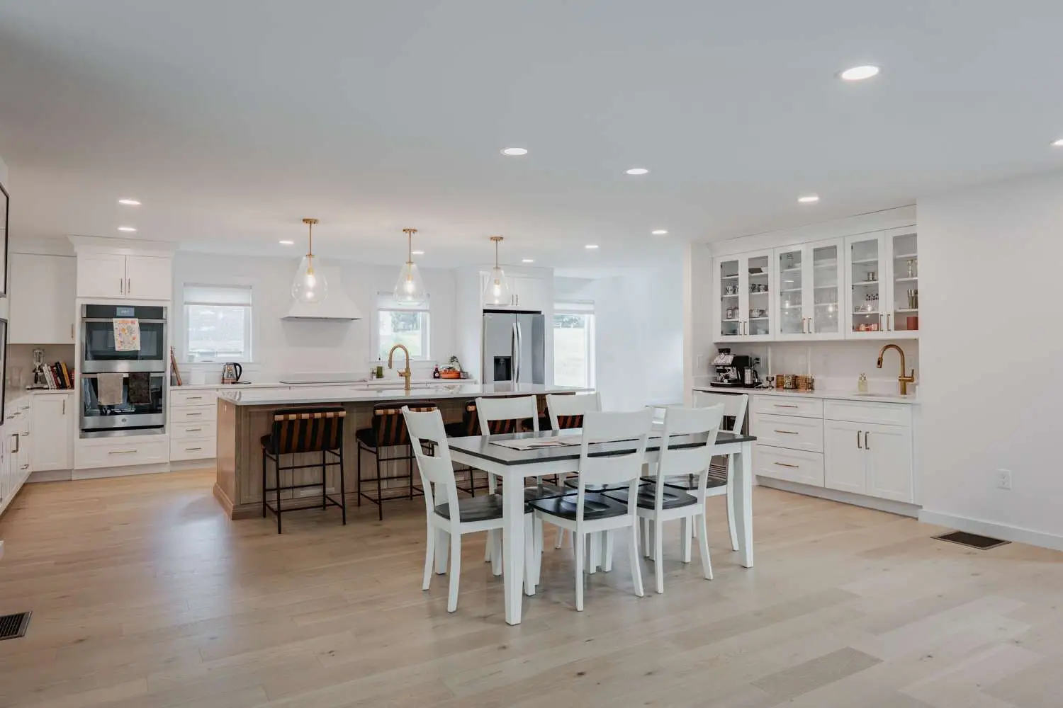 Modern kitchen interior featuring white cabinetry, a central island with seating, and a dining table, showcasing a clean and functional design for custom home living.