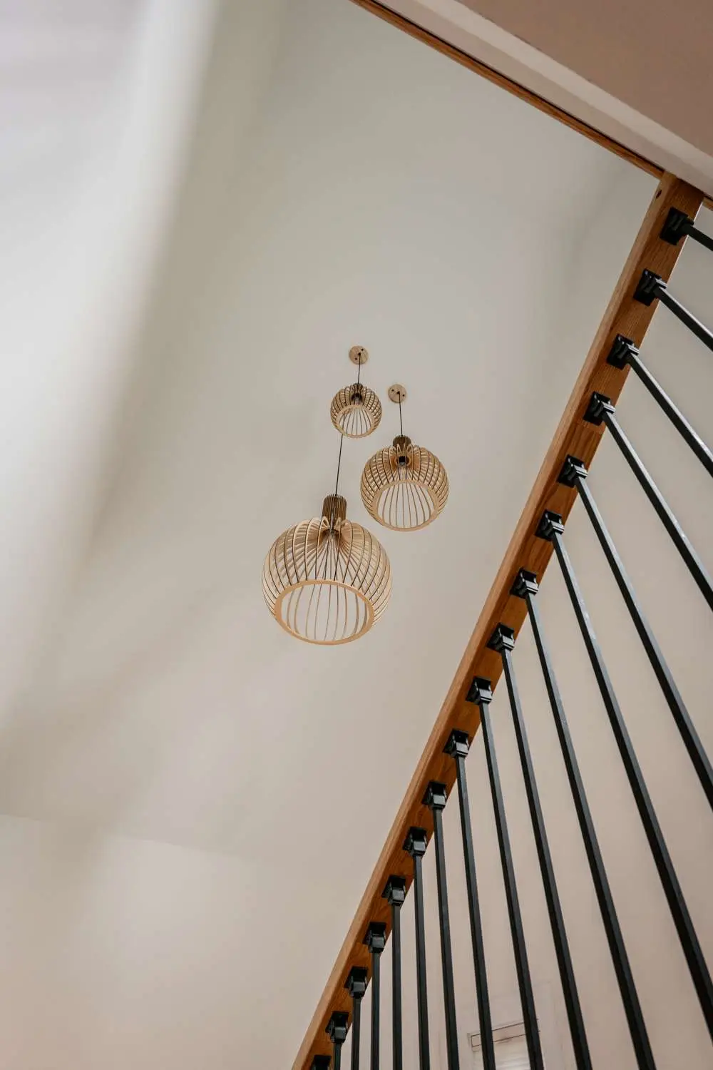 Hanging gold wire pendant lights above a staircase with black railings, showcasing modern interior design elements relevant to custom home builds by Bradford Construction Management.