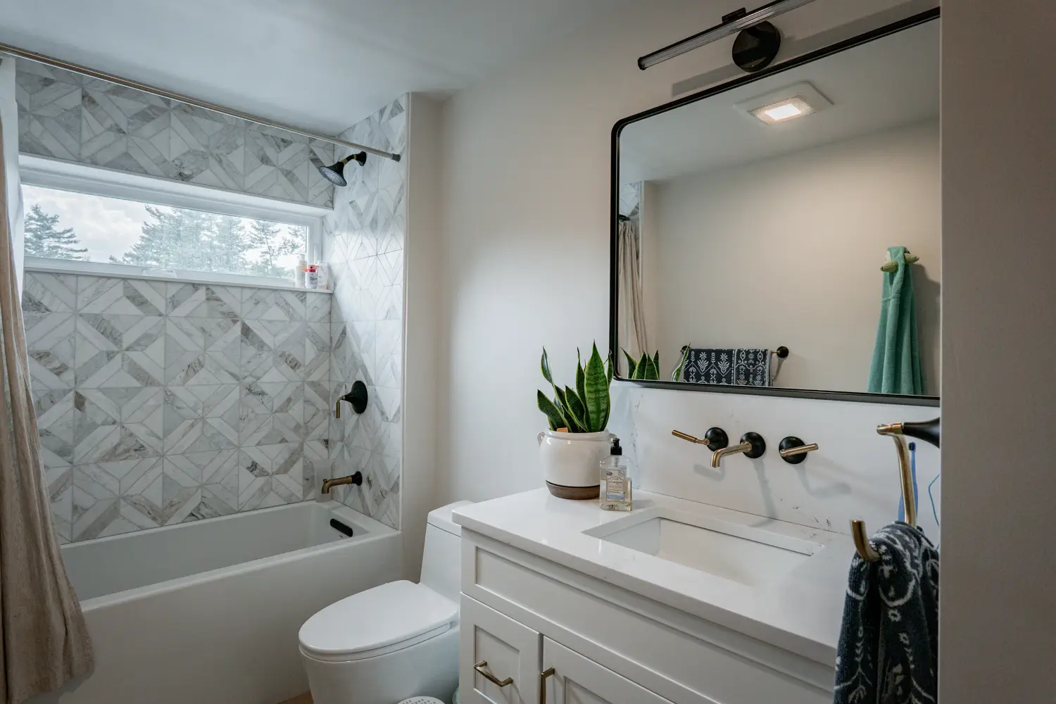 Modern bathroom featuring a stylish bathtub, geometric tile design, sleek black fixtures, and a white vanity with gold accents, showcasing quality craftsmanship and design.