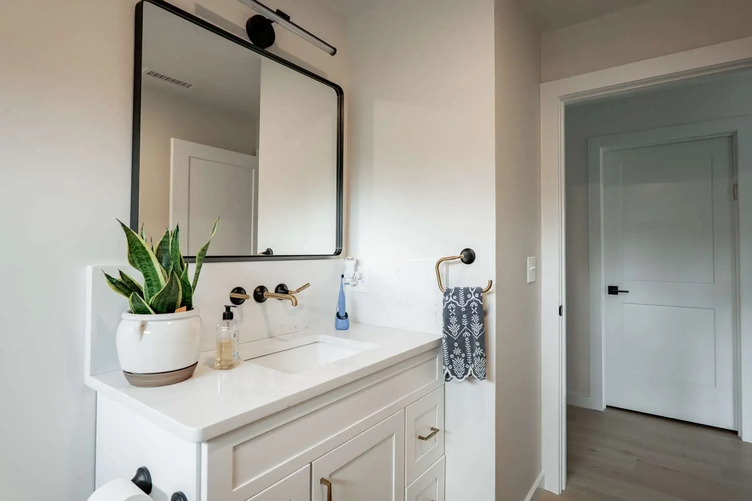 Modern bathroom design featuring a white vanity with gold fixtures, a large mirror, a potted snake plant, and a gray patterned towel, illustrating Bradford Construction's remodeling services.