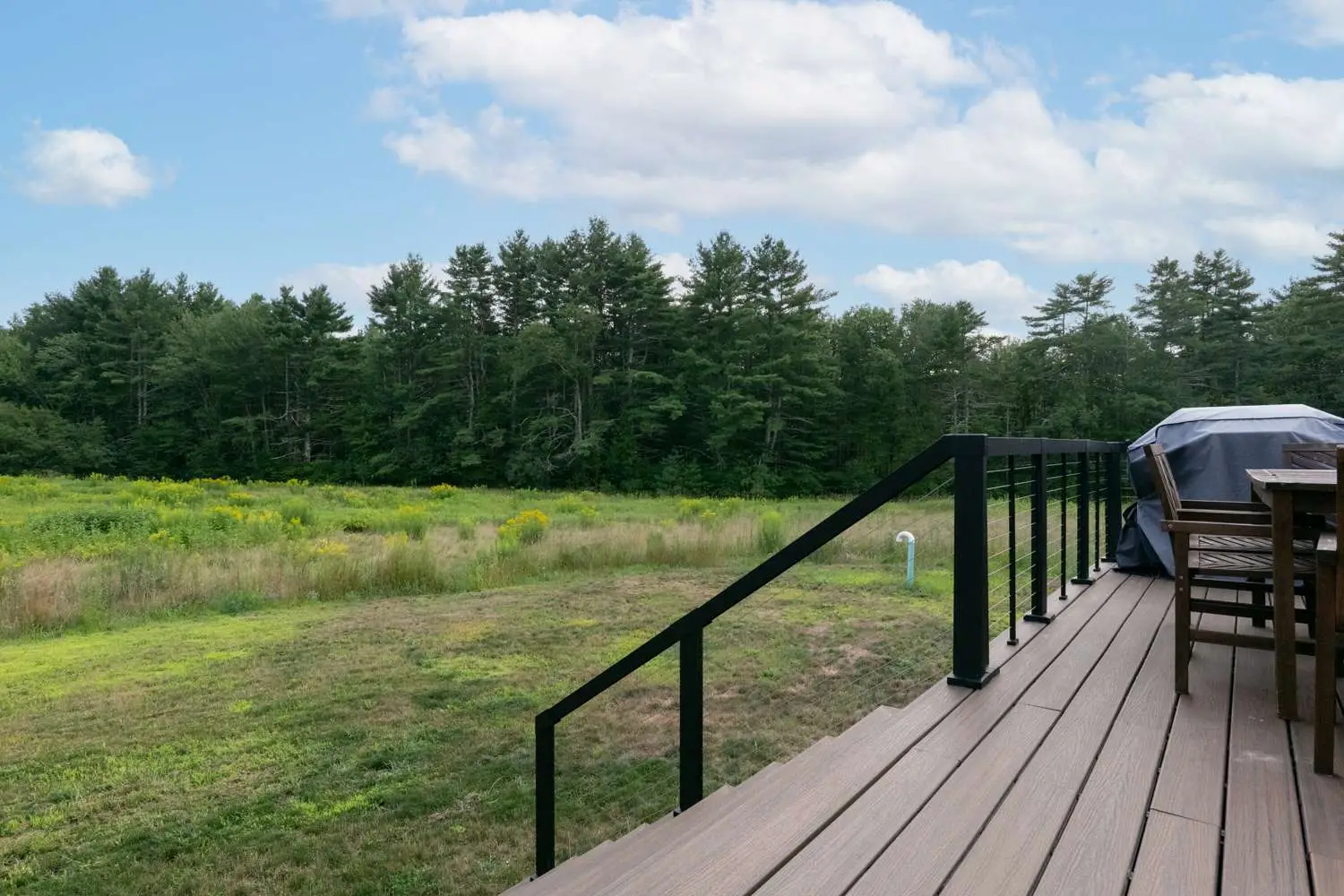 Deck view of a custom home in Exeter, NH, showcasing open green space and wooded backdrop, highlighting outdoor living features.