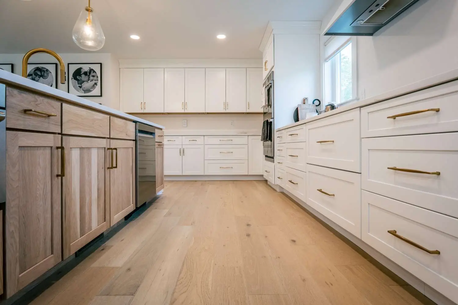Modern kitchen interior featuring a blend of light wood and white cabinetry with gold hardware, sleek countertops, and natural light illuminating the space.