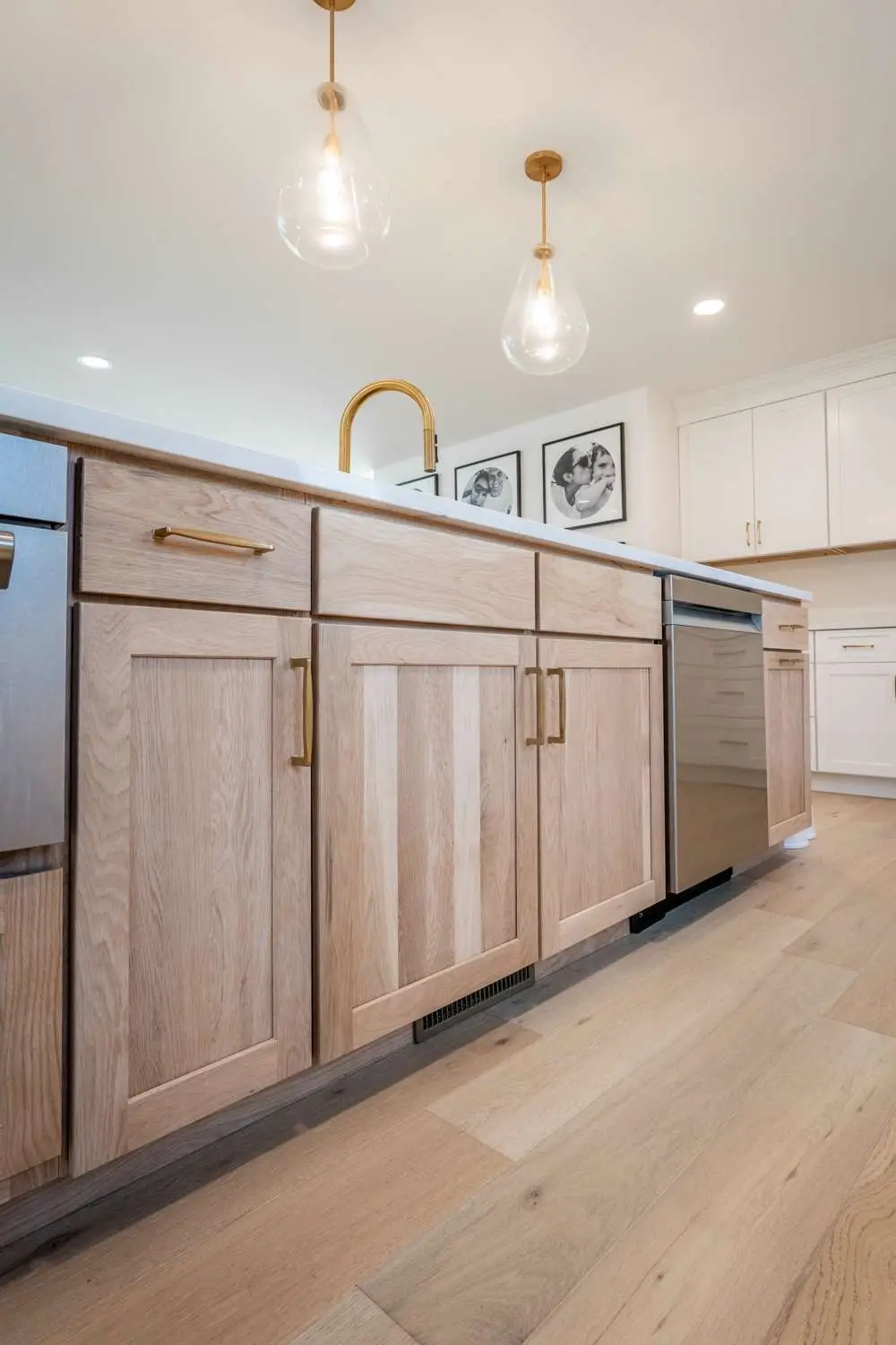 Modern kitchen cabinetry with light wood finish, gold hardware, stainless steel appliances, and pendant lighting, showcasing custom design features in a renovated home.