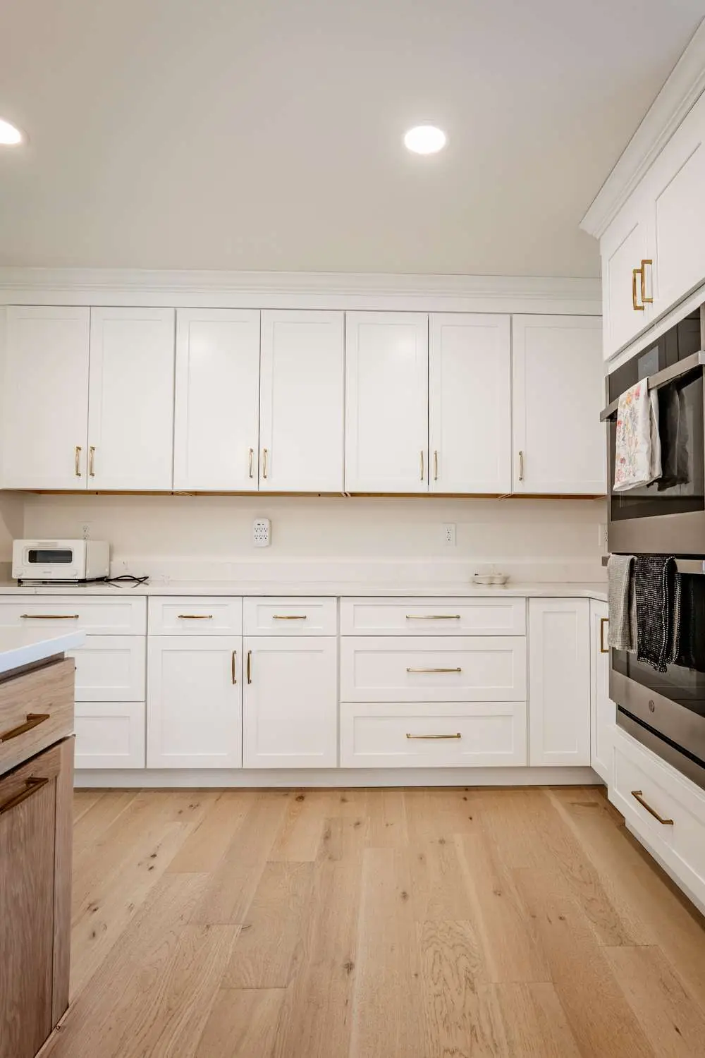 Modern kitchen design featuring white cabinetry with gold hardware, sleek countertops, and hardwood flooring, showcasing a custom home build by Bradford Construction Management in Exeter, NH.