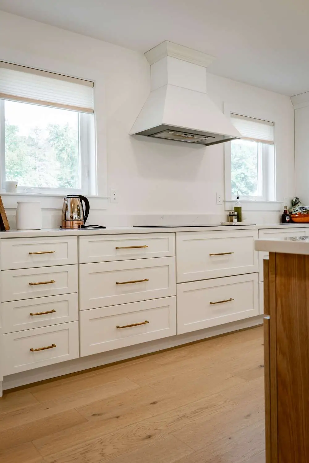 Modern kitchen design featuring white cabinetry with gold hardware, sleek range hood, and natural wood accents, showcasing custom home build aesthetics in Exeter, NH.