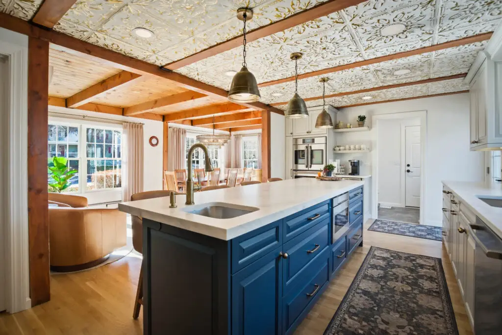 Modern kitchen interior with blue cabinetry, white countertops, decorative ceiling, and dining area, showcasing renovation ideas for enhancing home spaces.