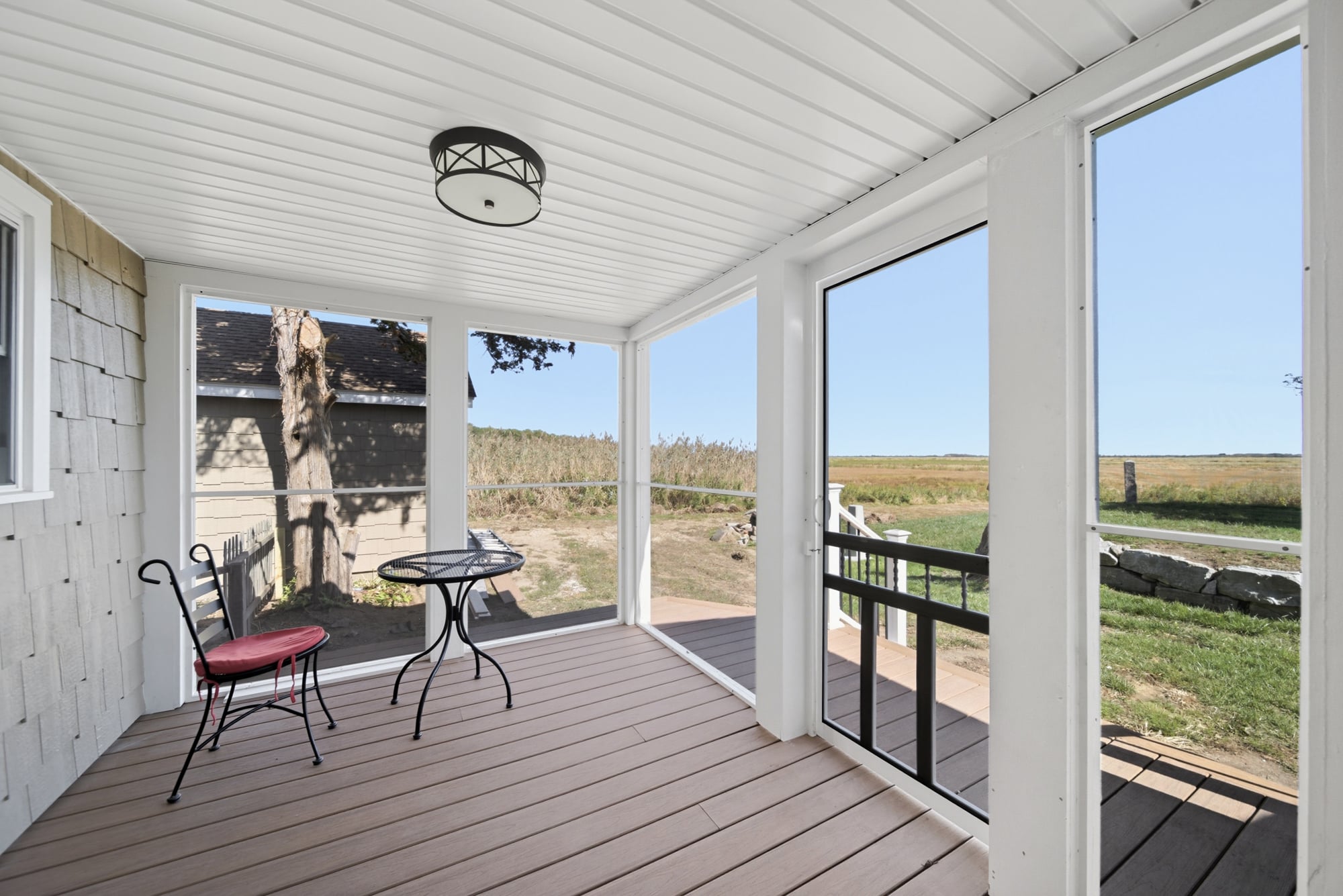 Screened porch featuring a bistro table and chair, with composite decking and views of marshland, designed for outdoor comfort in a flood-prone area.