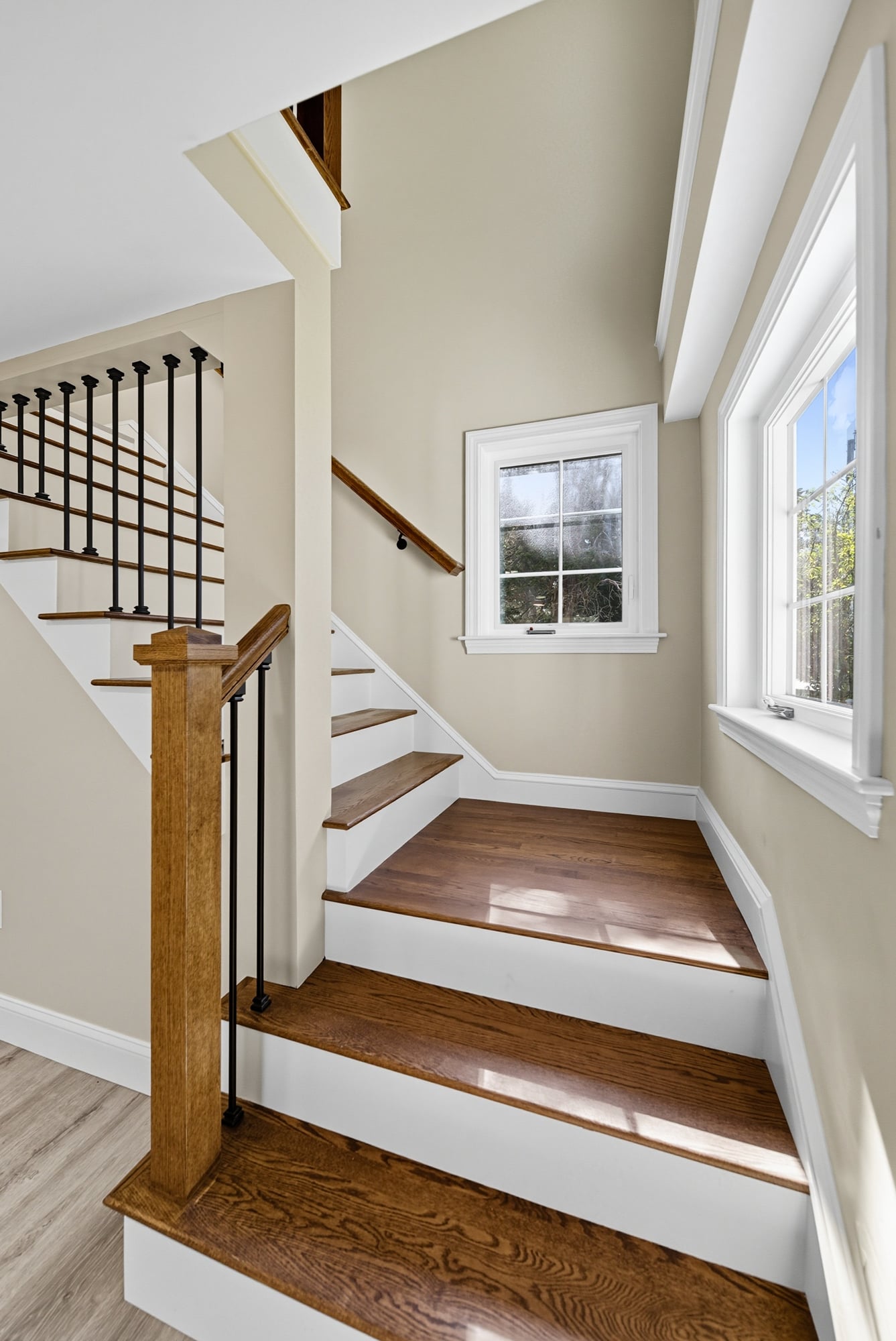 Staircase with new wood treads and risers, featuring an updated railing and natural light from a nearby window, highlighting the renovated interior space of a home in West Newbury, MA.