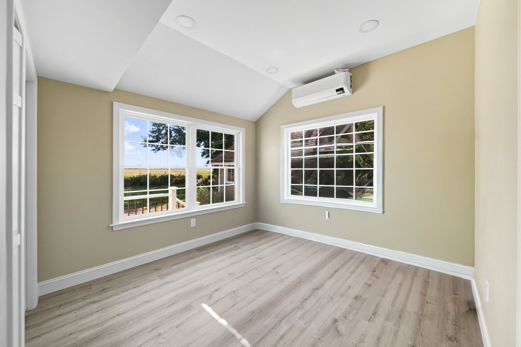 Bedroom with corner windows, mini-split heat pump, and light wood flooring, showcasing ocean views and newly renovated space in West Newbury, MA.