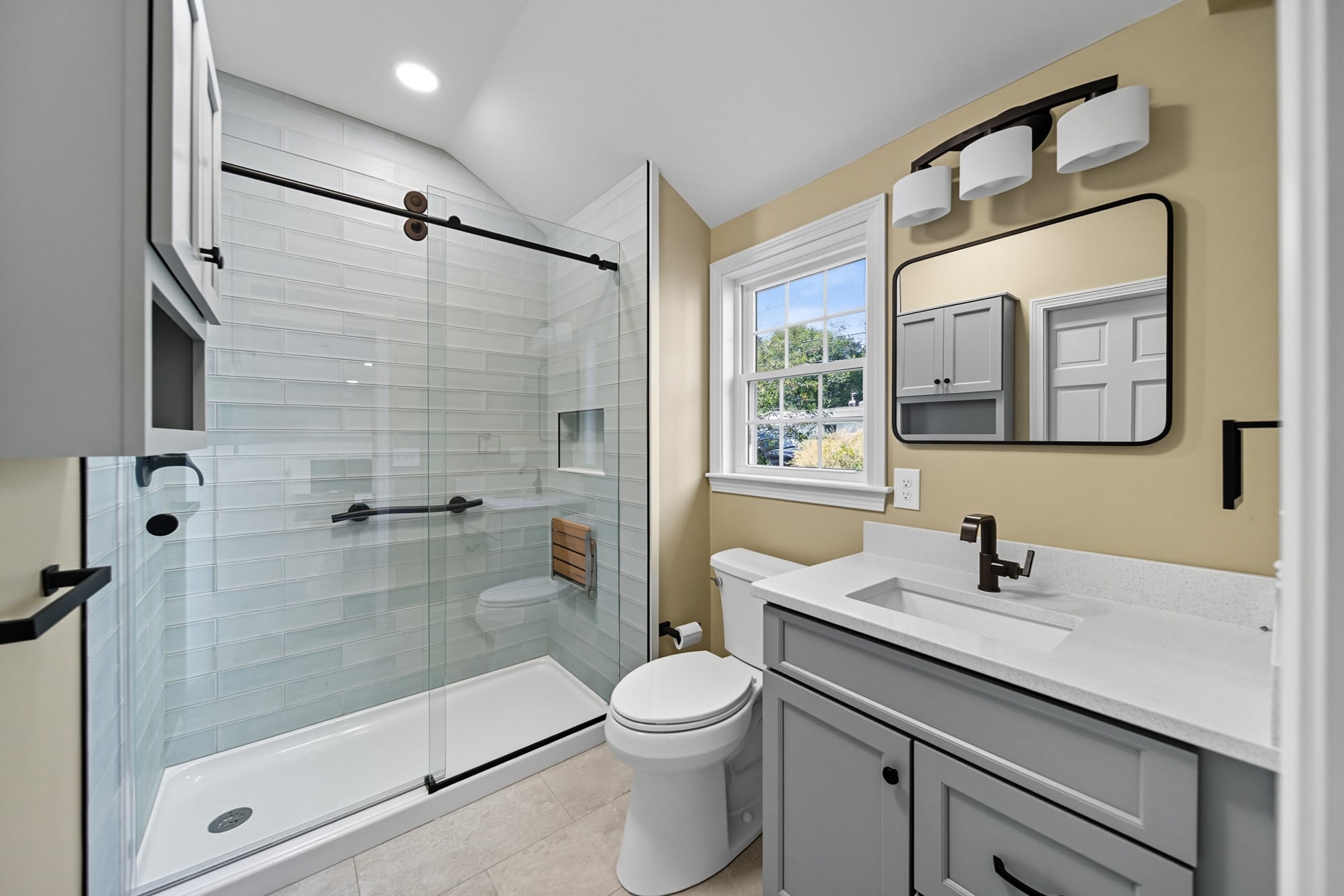 Modern bathroom with fully tiled shower, new vanity, sleek fixtures, and large window showcasing views, part of a home renovation project by Bradford Construction Management.