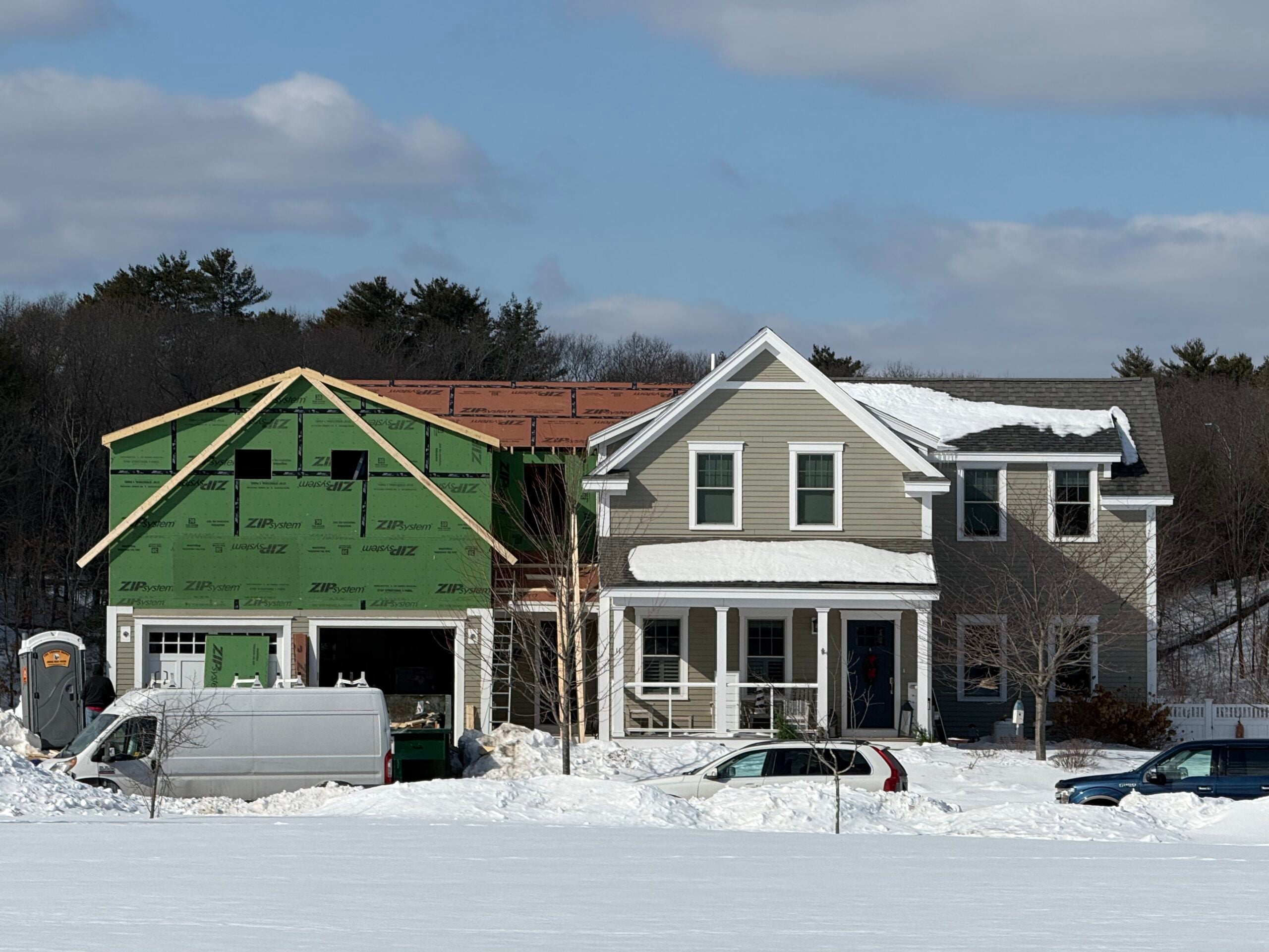 Home under construction with green ZIP system sheathing, adjacent to completed house, surrounded by snow, showcasing residential design-build process in Eastern MA.