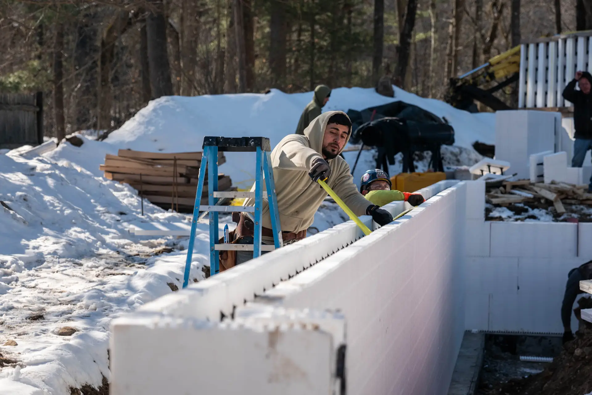 Construction workers measuring and installing insulated concrete forms at an active ADU job site in Haverhill, MA, with snow-covered ground and a modern open floor plan under development.