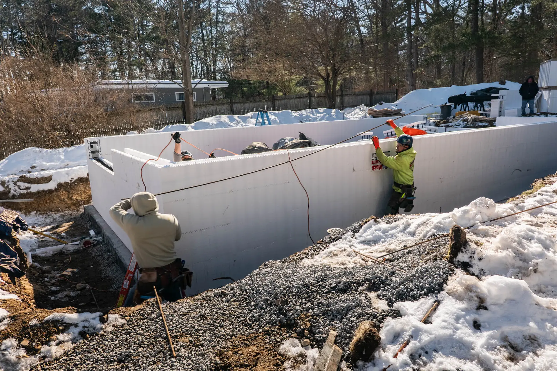 Construction workers installing insulated concrete forms for an ADU foundation, surrounded by snow and gravel, showcasing residential construction services by Bradford Construction Management.