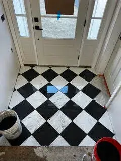 Black and white checkered tile entryway in newly constructed accessory dwelling unit in Essex, MA, featuring buckets of grout and tools.