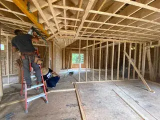 Interior framing construction of an accessory dwelling unit in Essex, MA, featuring workers installing wall studs and overhead beams in an open layout.