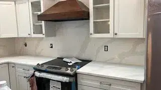 Open kitchen featuring white shaker cabinetry, marble backsplash, natural wood range hood, and quartz countertops in an accessory dwelling unit in Essex, MA.