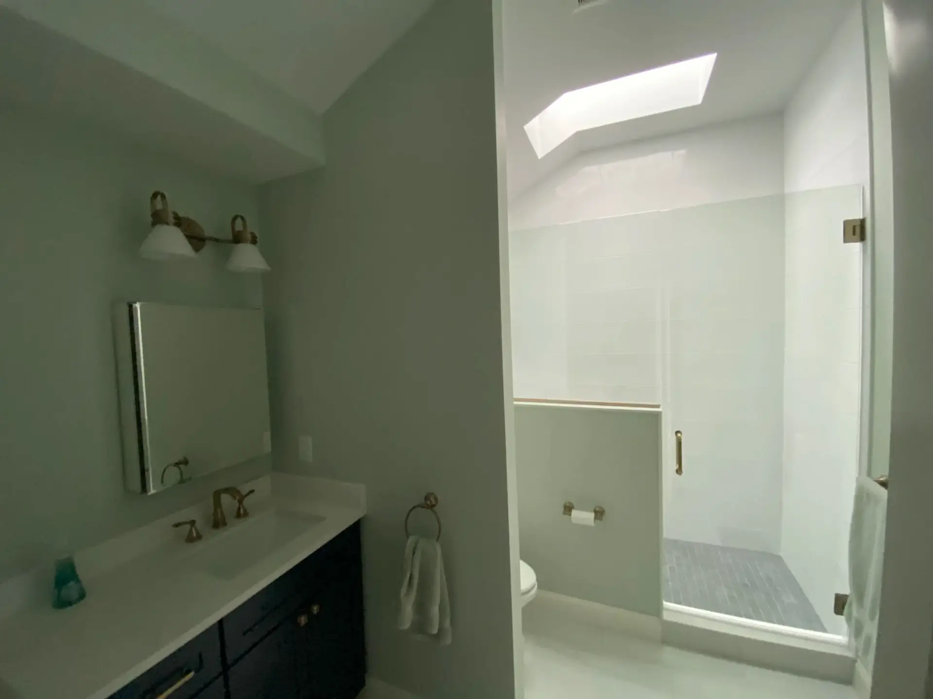 Custom bathroom vanity with gold fixtures, skylight shower with glass enclosure, and modern design elements in a newly built home in Wakefield, MA.