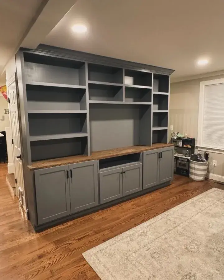 Built-in shelving unit with gray cabinetry and wooden countertop in a modern living room, showcasing custom storage solutions for a residential construction project in Wakefield, MA.