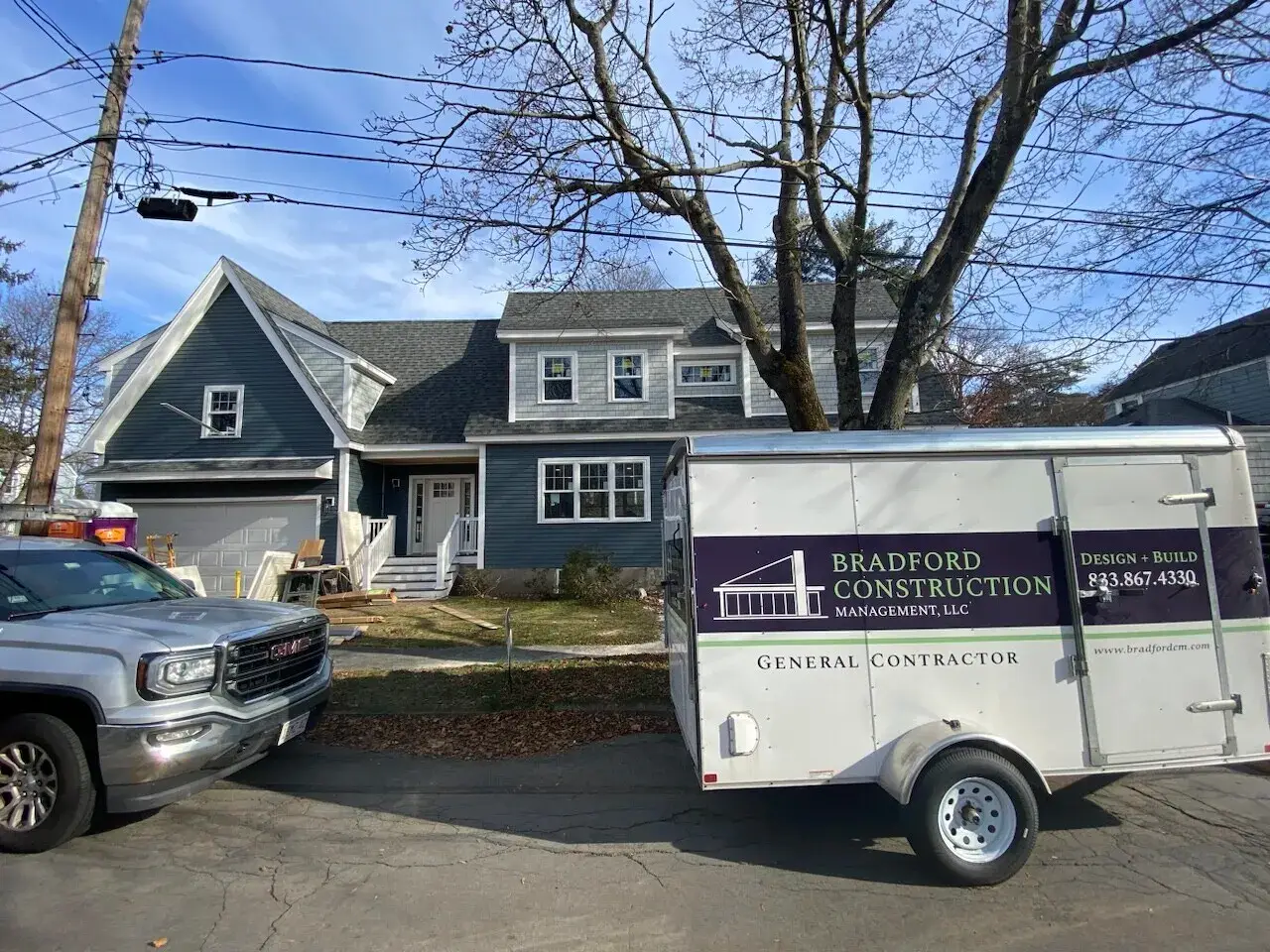 Custom home exterior in Wakefield, MA featuring blue clapboard siding, front steps, and a Bradford Construction trailer parked nearby, showcasing the completed residential project.