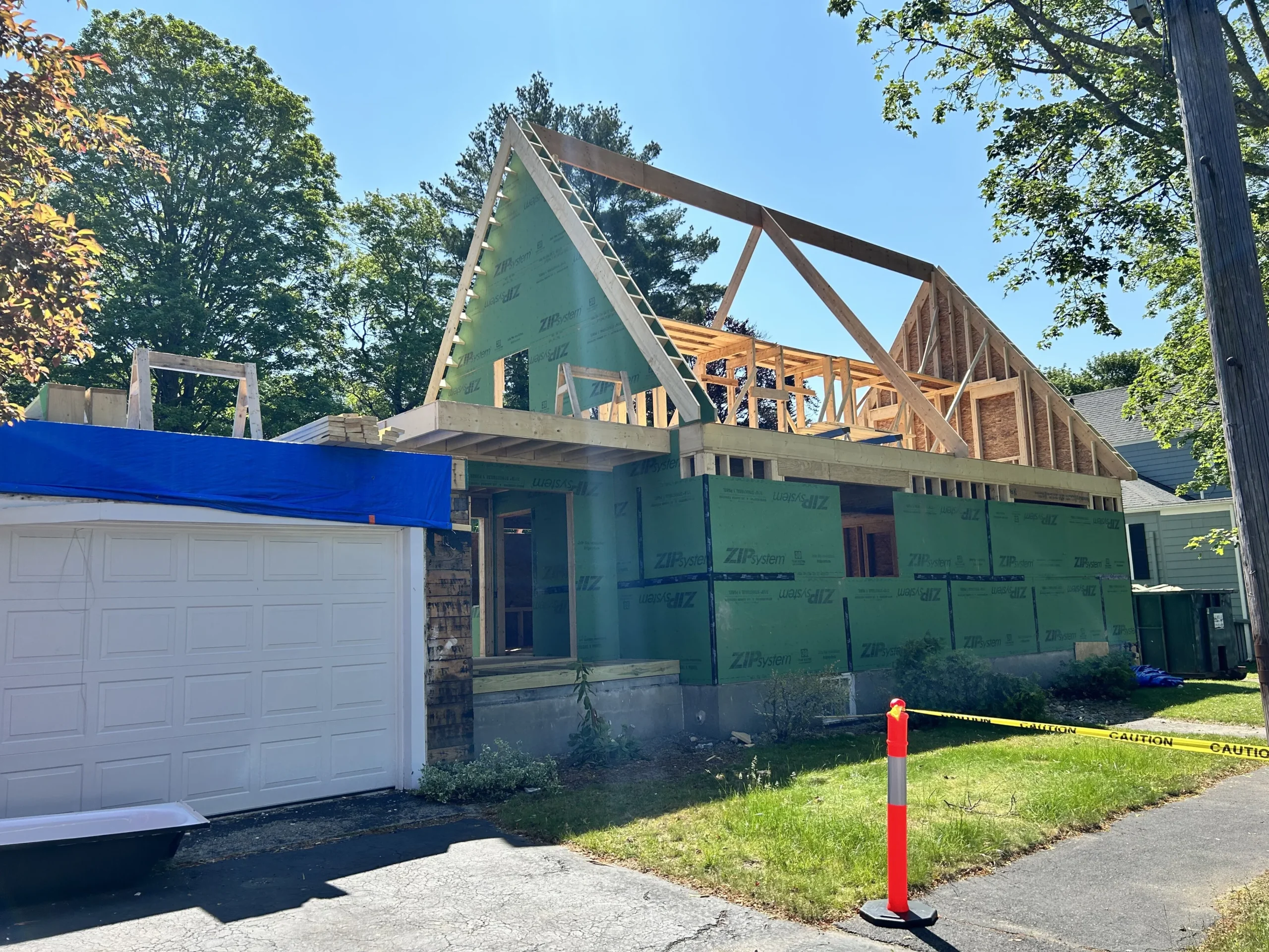 Custom home construction in Wakefield, MA, featuring engineered roof trusses, ZIP sheathing, and a partially completed exterior with blue tarp covering.