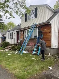 Workers removing old siding from a custom home in Wakefield, MA, showcasing the demolition phase of the renovation process, with a blue ladder and debris on the ground.