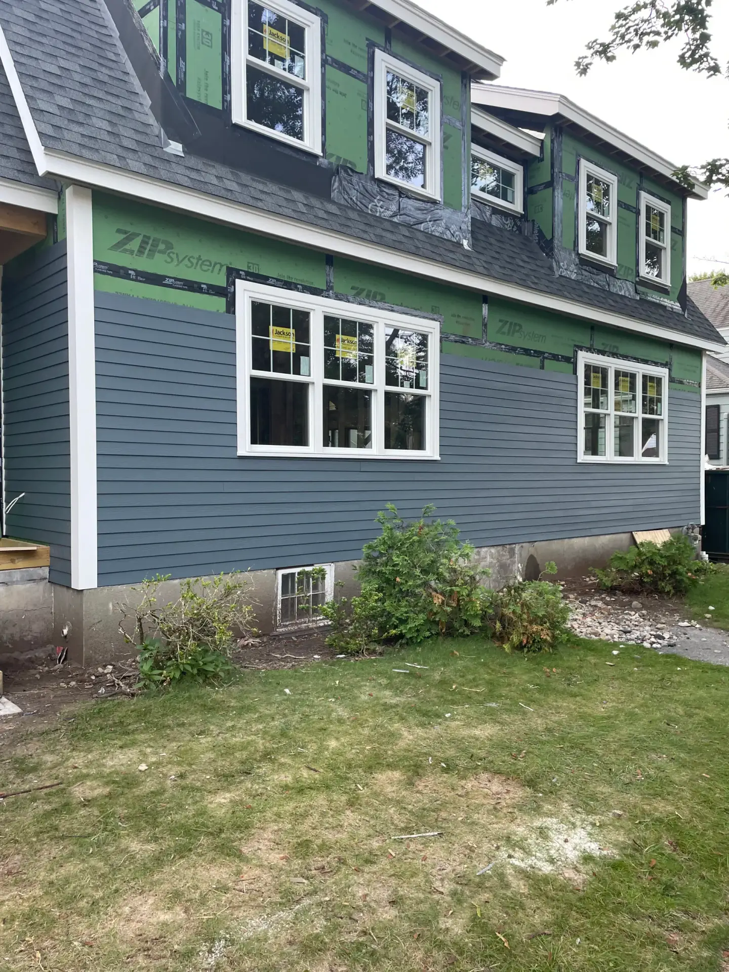 Custom home exterior in Wakefield, MA featuring blue clapboard siding, ZIP sheathing, and new windows, showcasing construction progress for a residential build by Bradford Construction.
