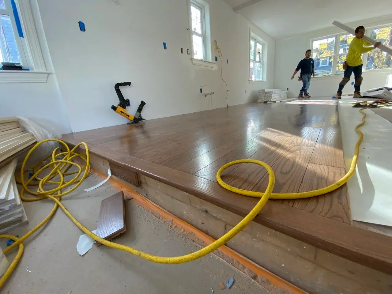 Hardwood floor installation in a custom home in Wakefield, MA, featuring workers, yellow extension cord, and unfinished walls.