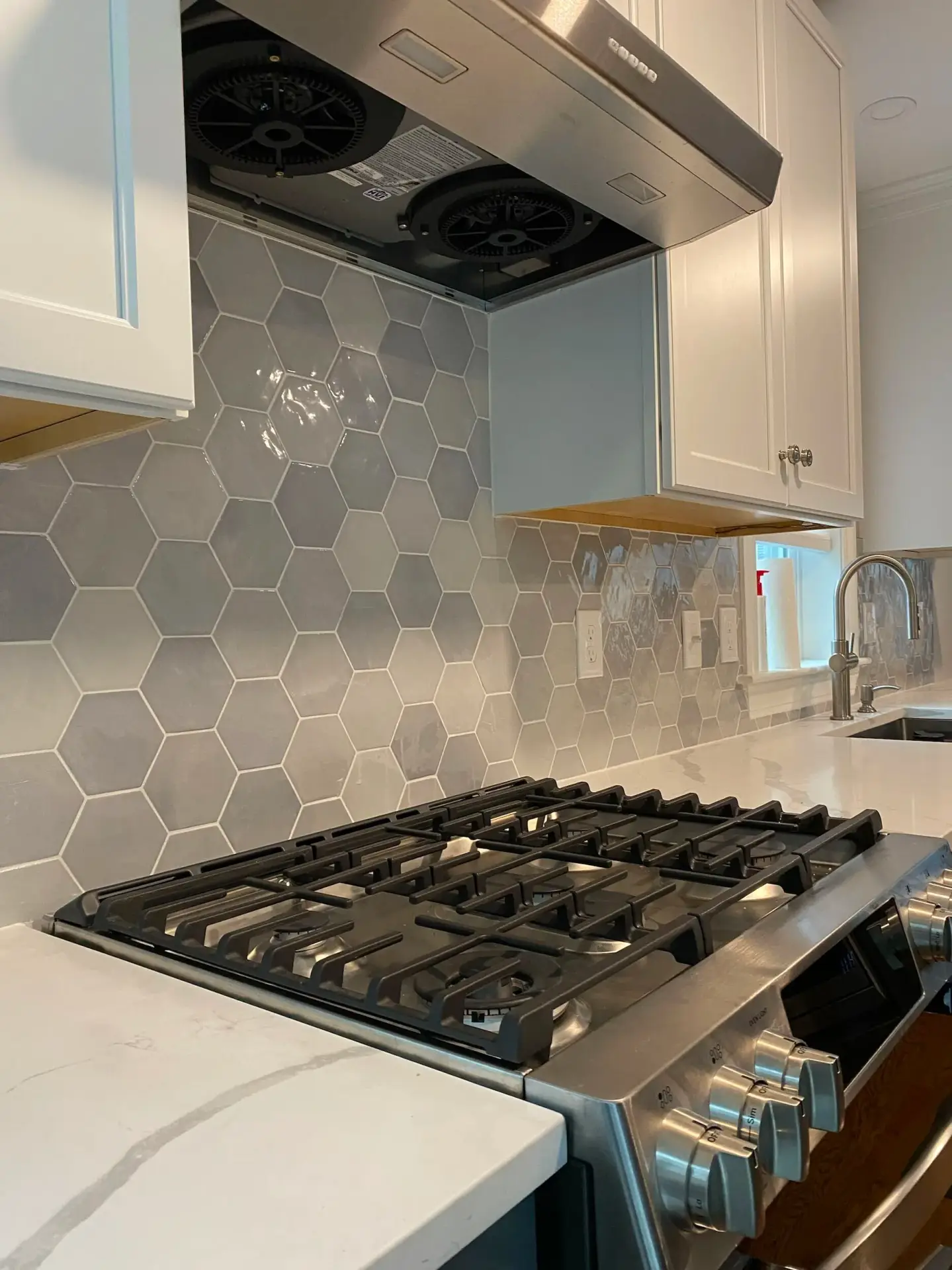 Custom kitchen featuring hexagon-tile backsplash, gas cooktop, and modern cabinetry in a residential home build.