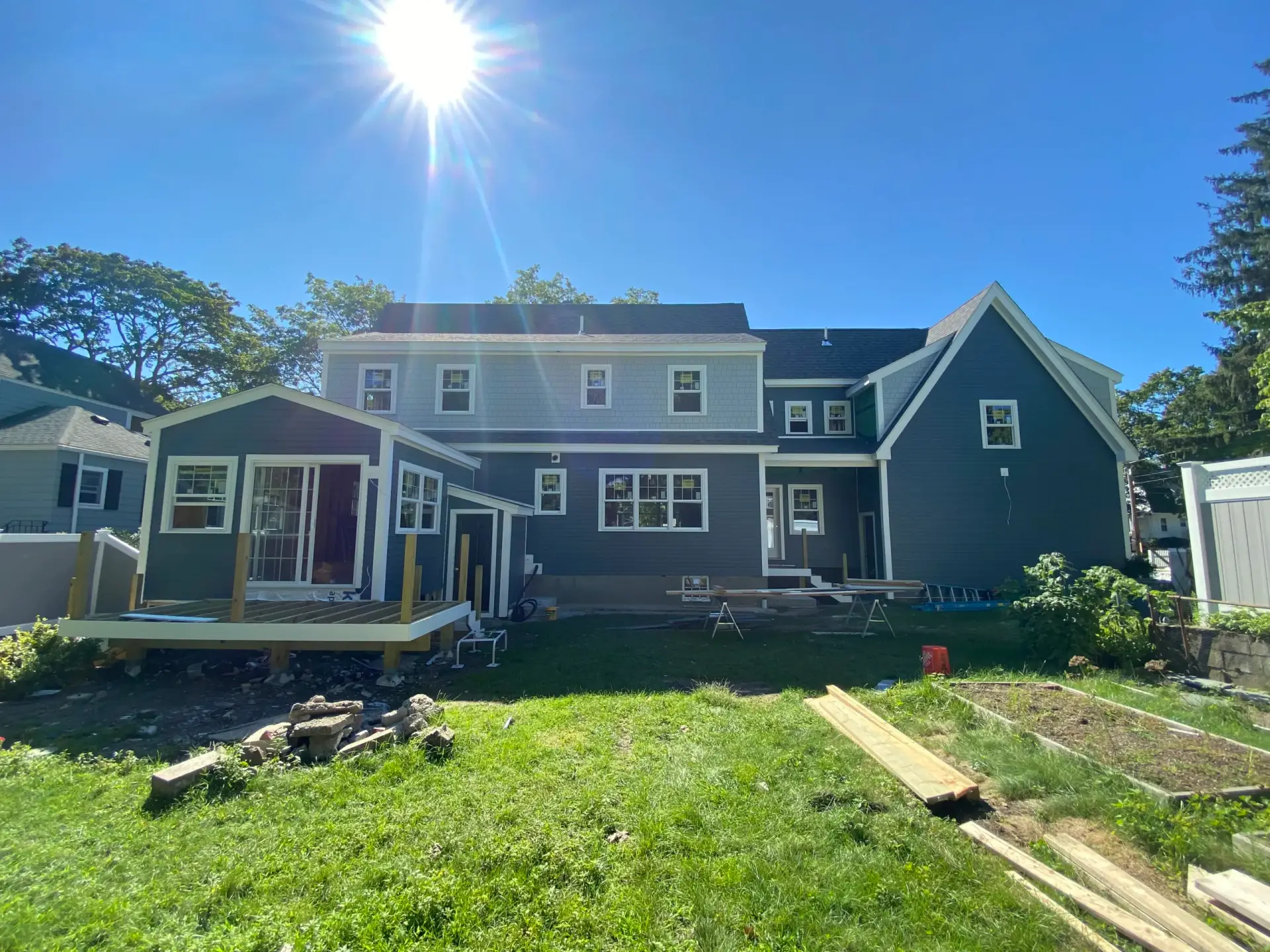 Custom home exterior in Wakefield, MA featuring blue clapboard siding, newly added rear deck, and landscaped yard with construction materials.