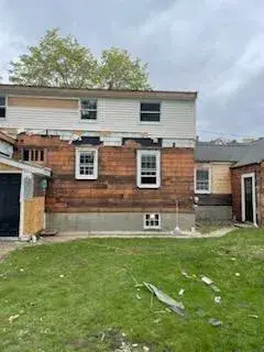 Rear exterior of a custom home in Wakefield, MA, showing pre-renovation condition with exposed wood and siding, indicating ongoing demolition and framing work.