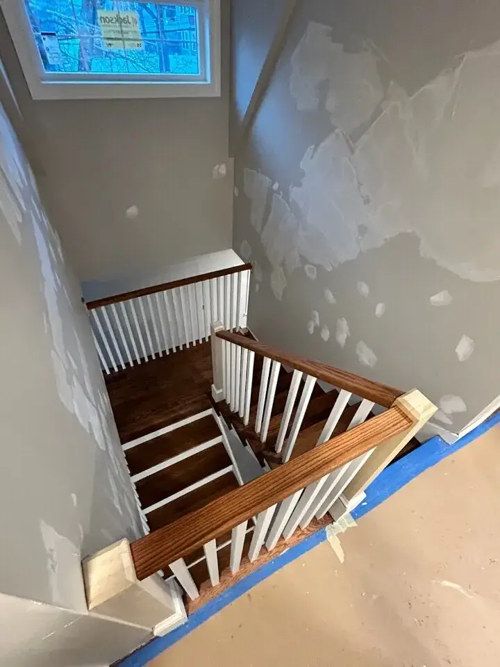 Custom staircase with oak railing and hardwood floors in a newly constructed home in Wakefield, MA, showcasing drywall finishing and natural light from a window.