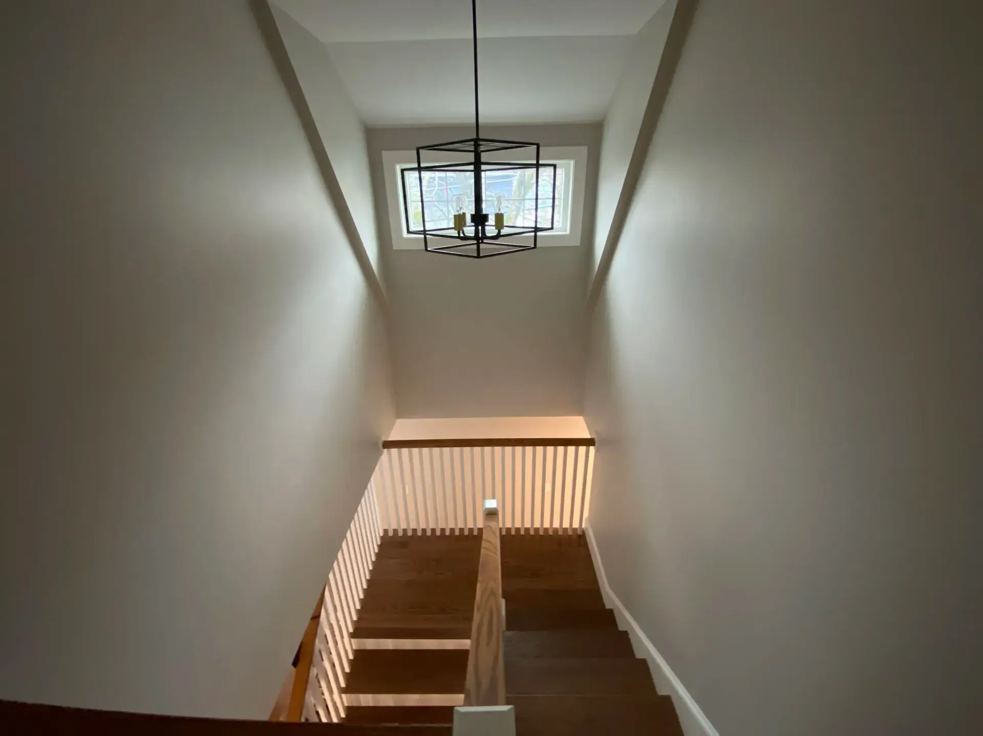 Custom staircase with oak railing and pendant lighting in a newly built home in Wakefield, MA, showcasing modern design elements and natural light.